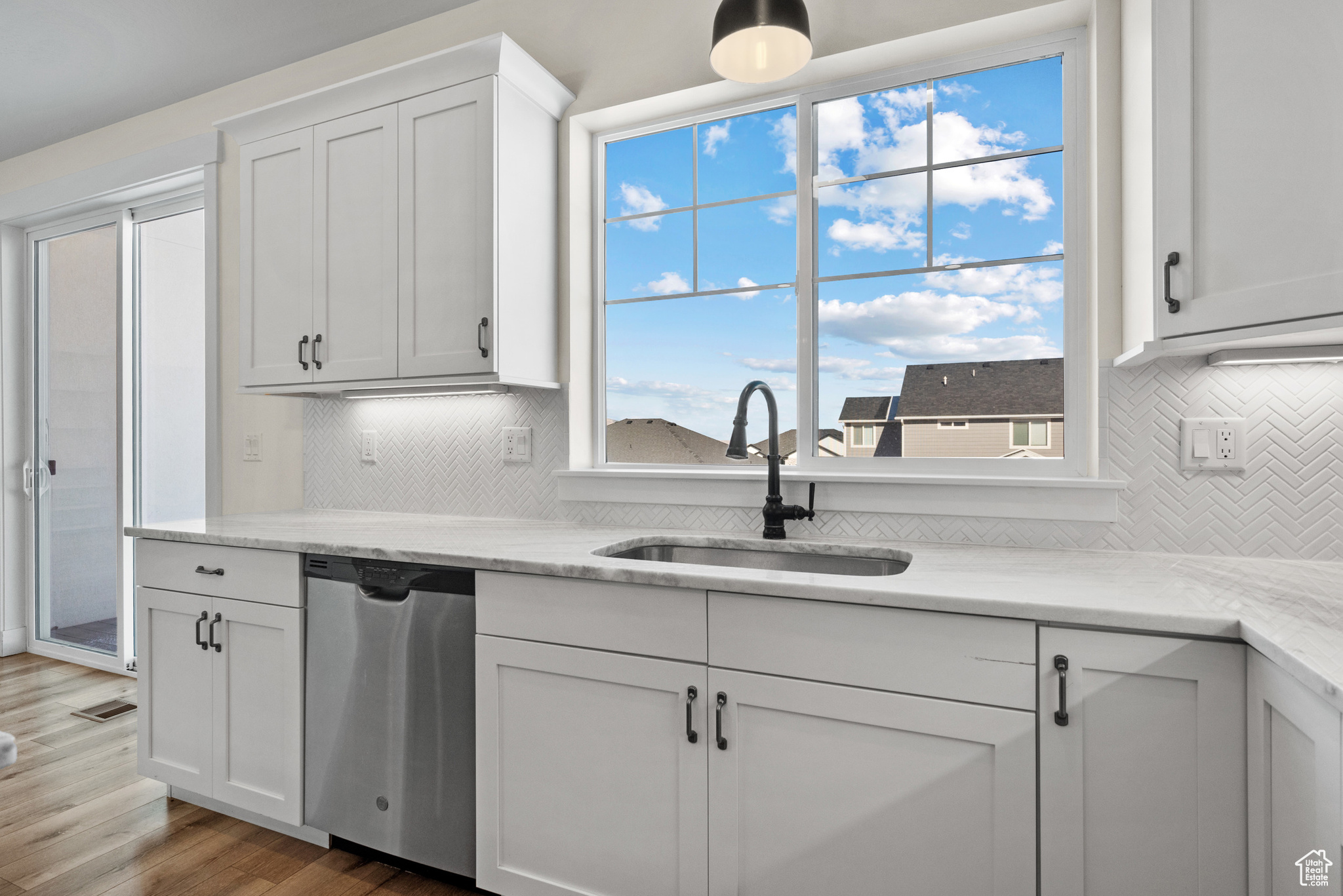 Kitchen with sink, light stone counters, wood-type flooring, white cabinets, and stainless steel dishwasher