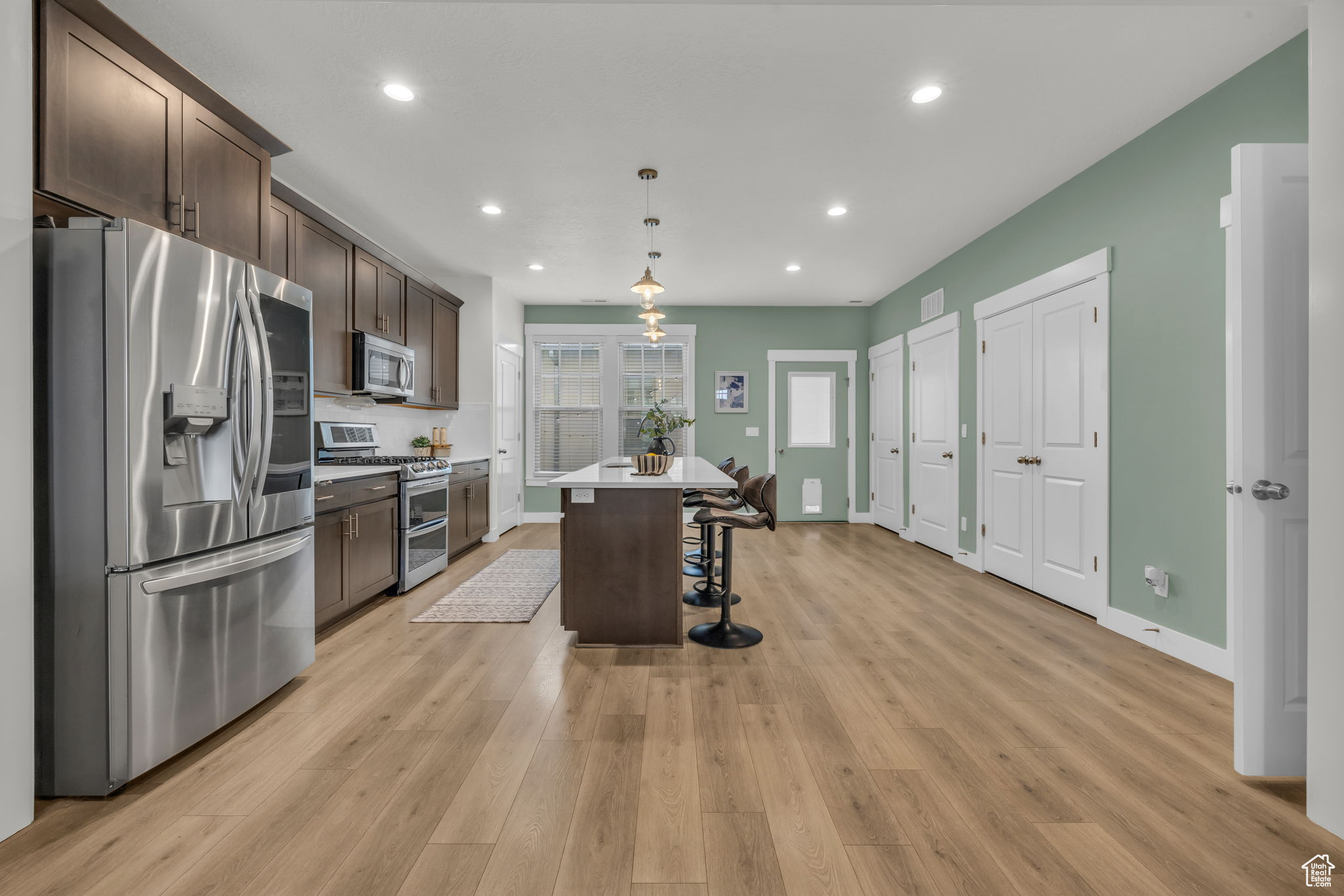 Kitchen featuring a kitchen bar, dark brown cabinets, appliances with stainless steel finishes, a kitchen island, and pendant lighting