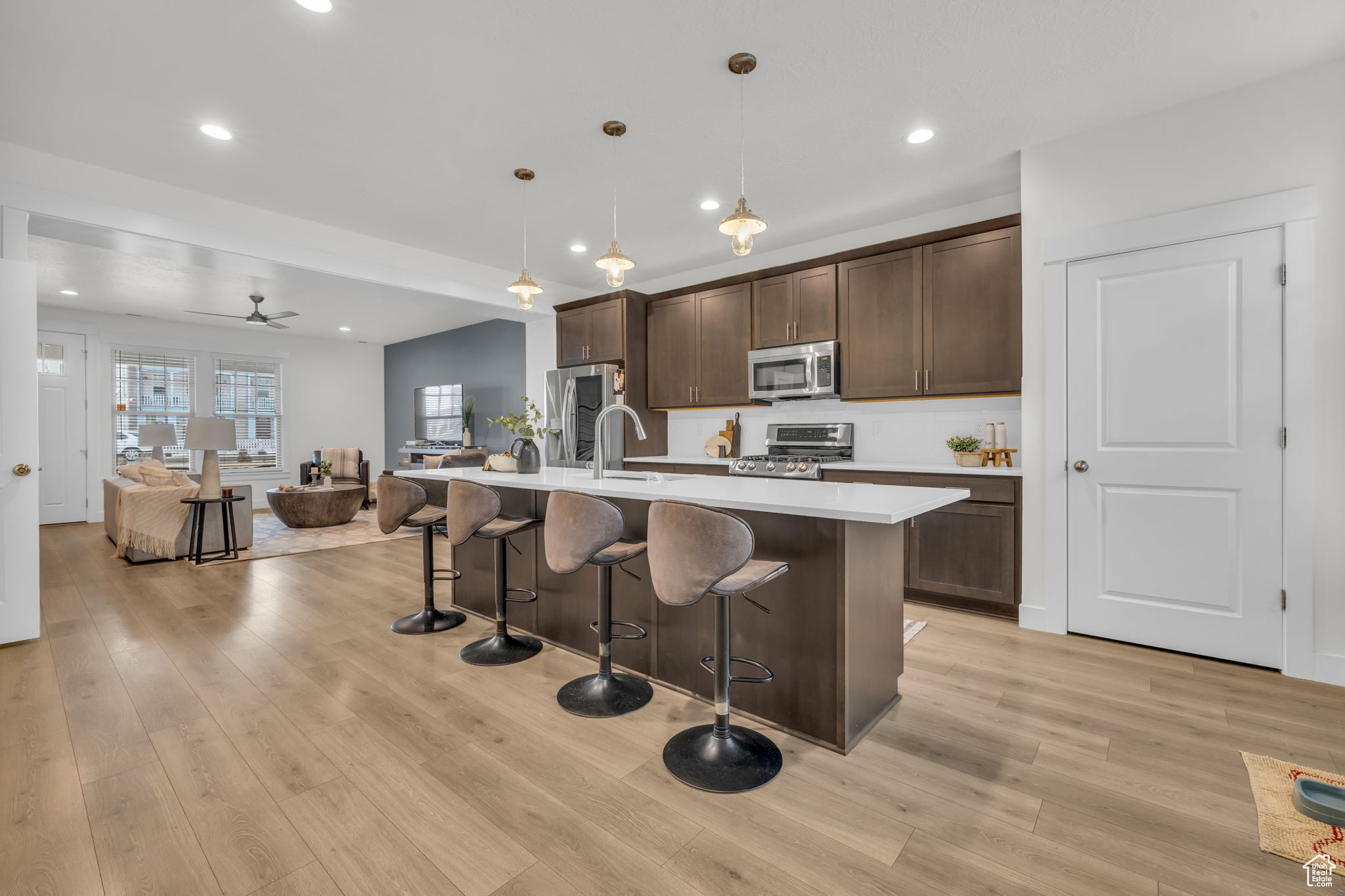 Kitchen with a breakfast bar area, appliances with stainless steel finishes, a kitchen island with sink, hanging light fixtures, and light hardwood / wood-style floors