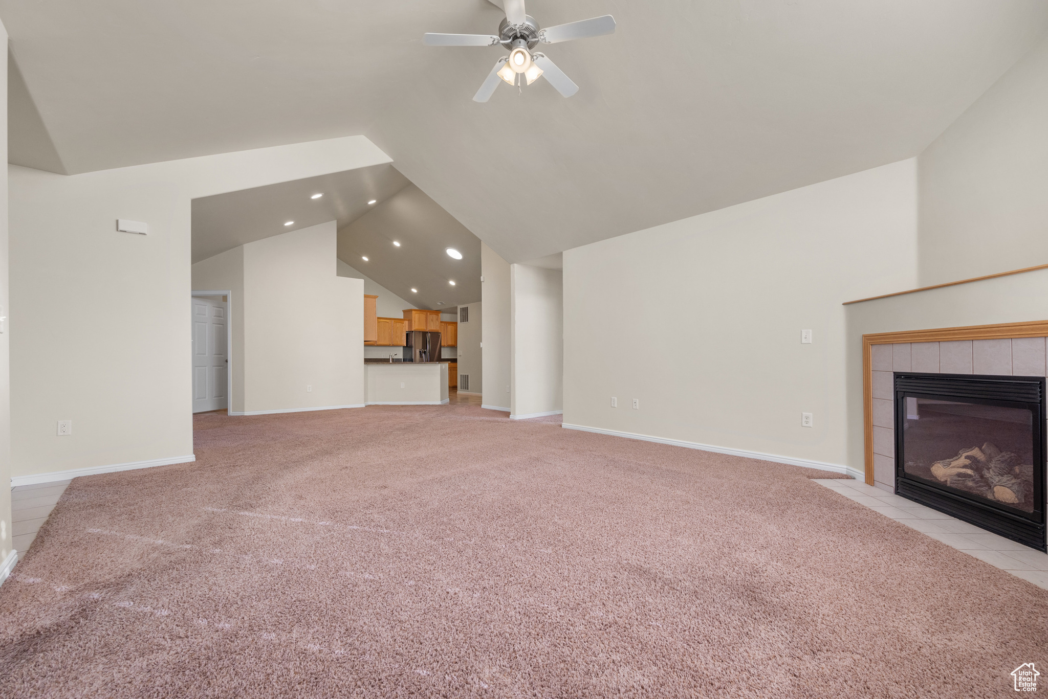 Unfurnished living room featuring light carpet, vaulted ceiling, a tile fireplace, and ceiling fan