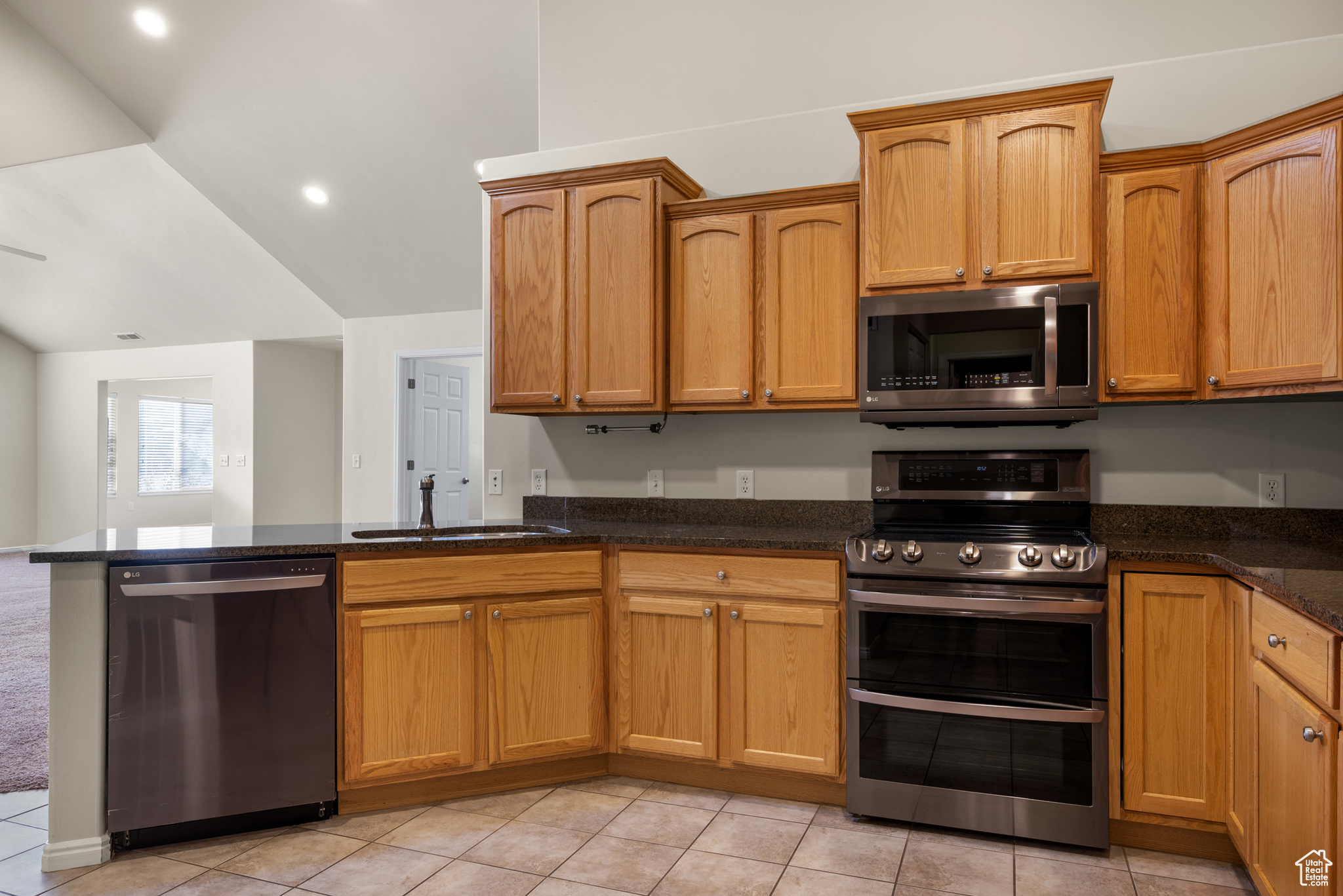 Kitchen featuring sink, dark stone countertops, stainless steel appliances, light tile patterned flooring, and vaulted ceiling