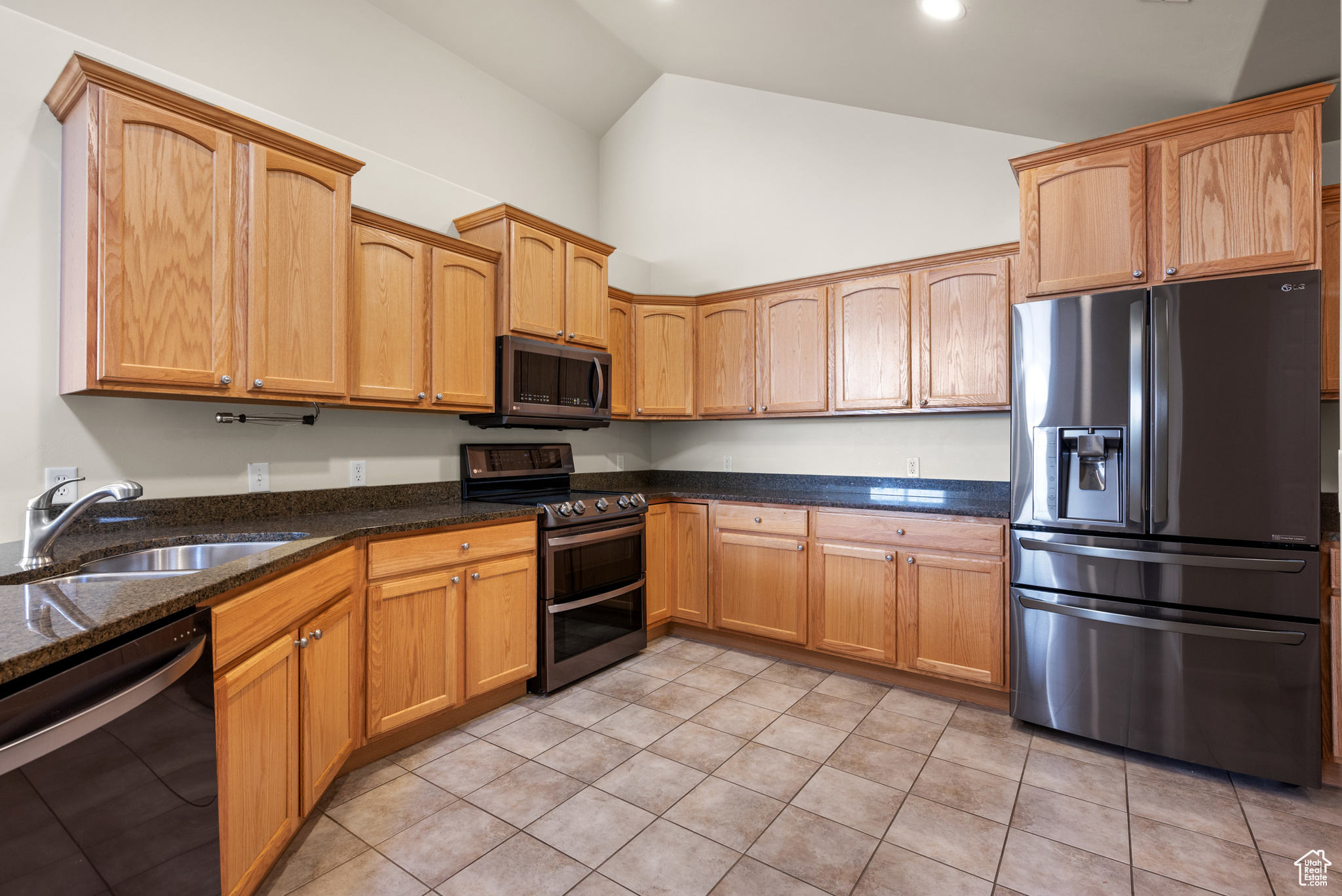 Kitchen with sink, light tile patterned floors, high vaulted ceiling, black appliances, and dark stone counters