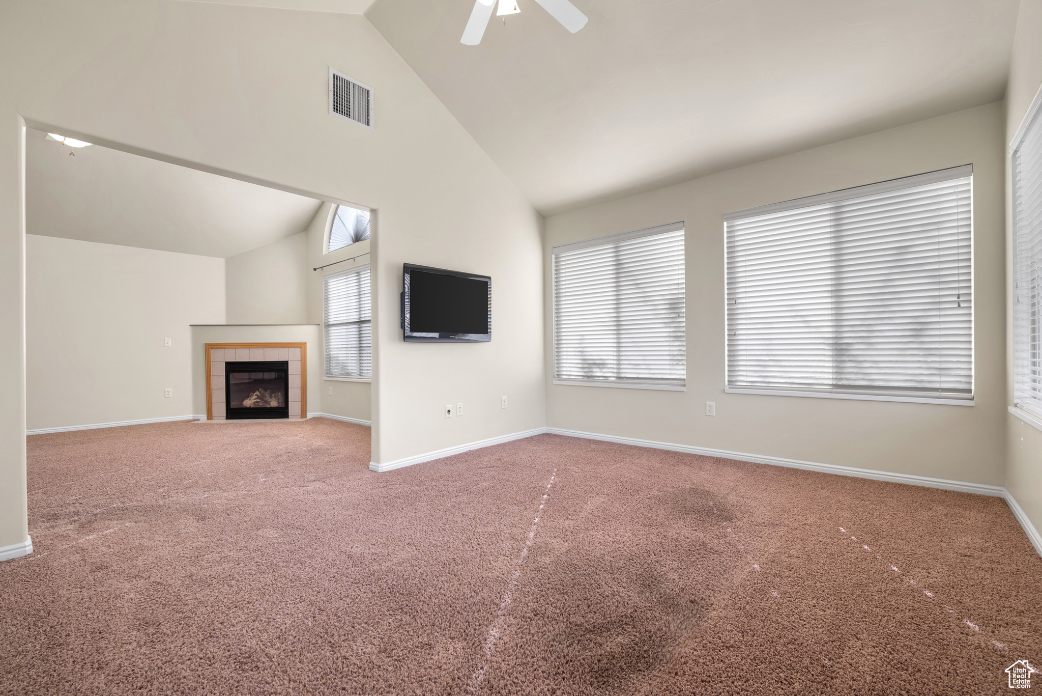 Unfurnished living room featuring a tile fireplace, carpet floors, ceiling fan, and high vaulted ceiling