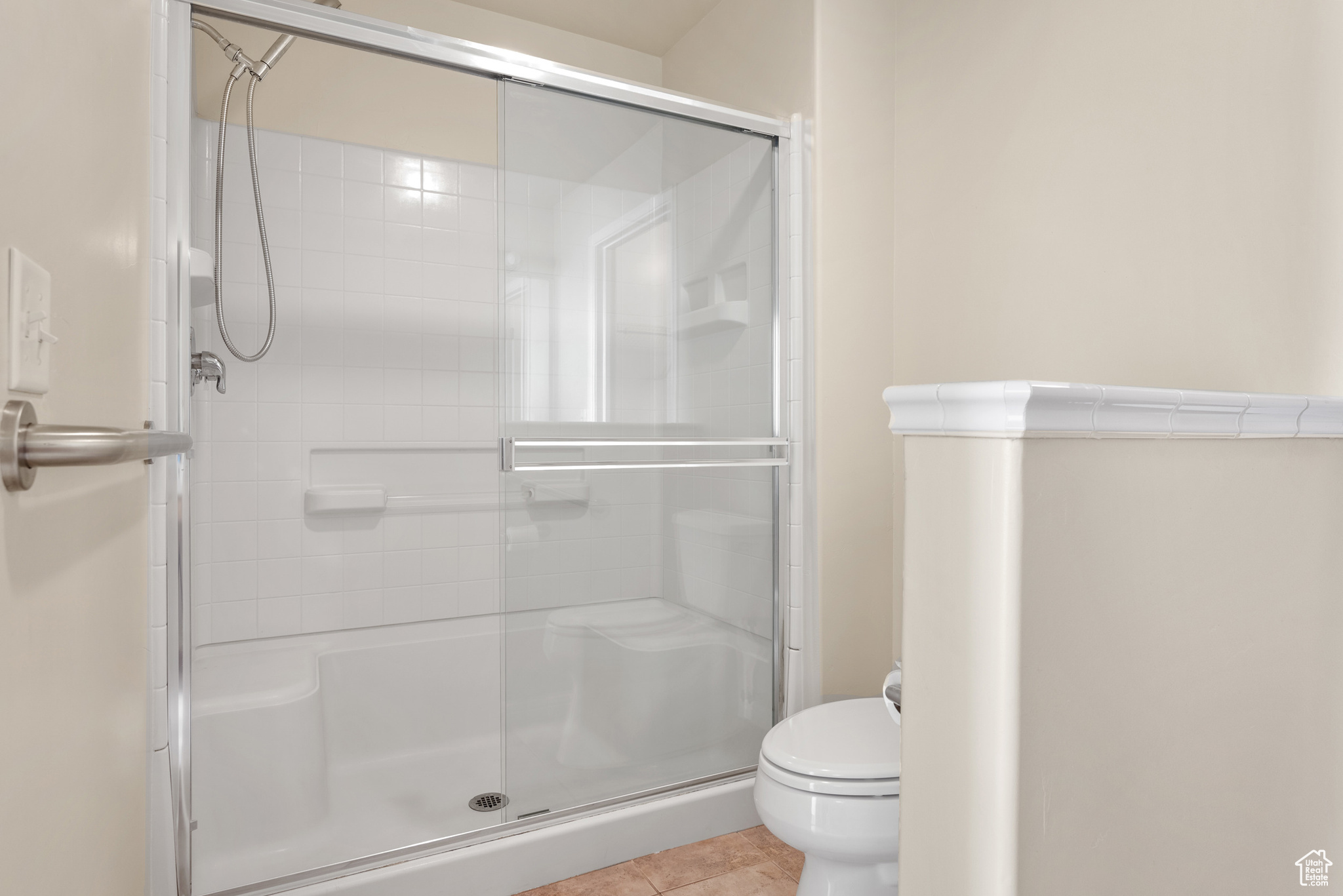 Bathroom featuring toilet, tile patterned flooring, and a shower with door