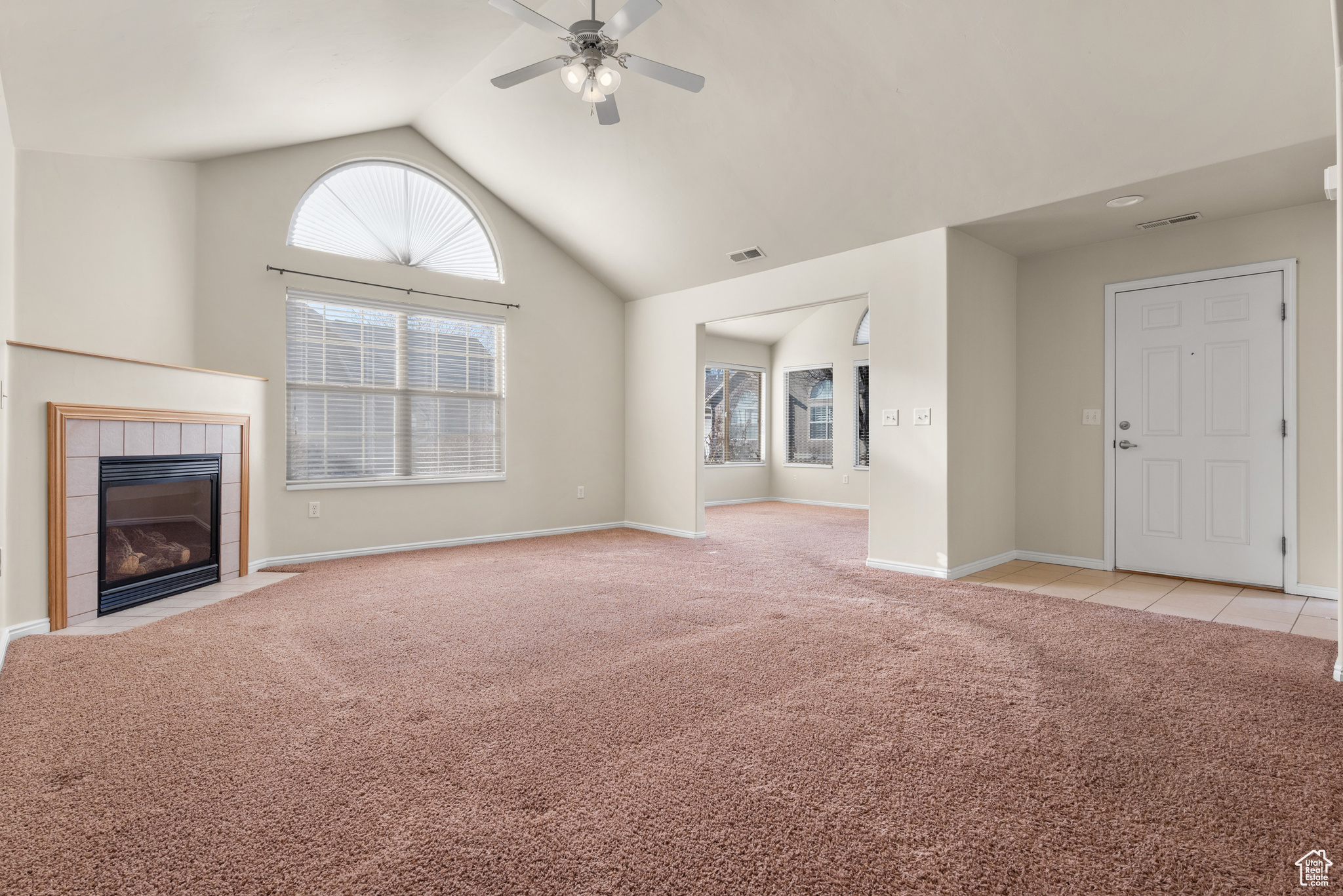 Unfurnished living room featuring lofted ceiling, light colored carpet, a tile fireplace, and ceiling fan