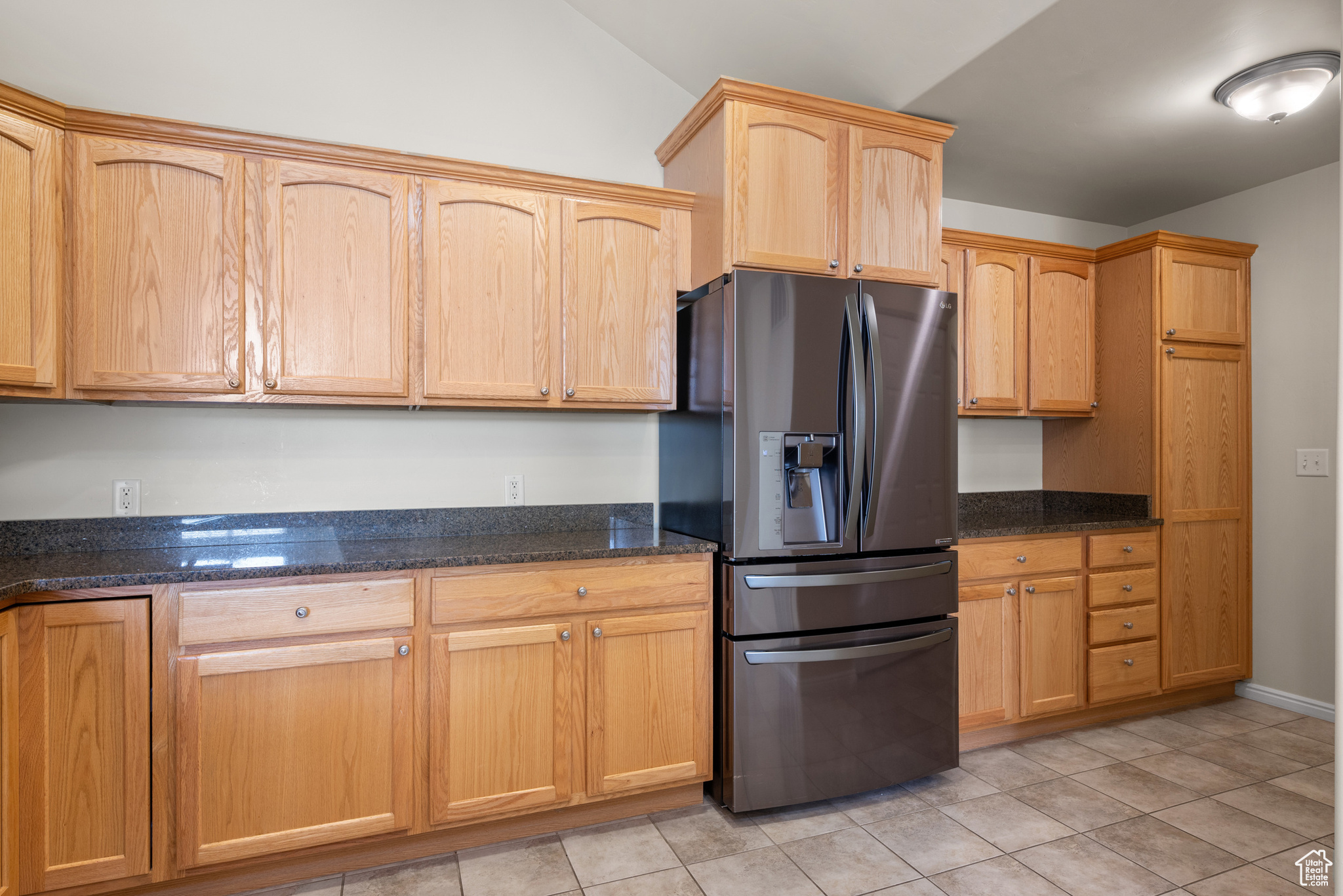 Kitchen with light tile patterned floors, stainless steel fridge, and dark stone counters