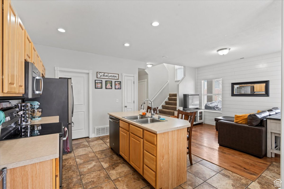 Kitchen featuring sink, a breakfast bar area, a kitchen island with sink, stainless steel appliances, and light brown cabinets