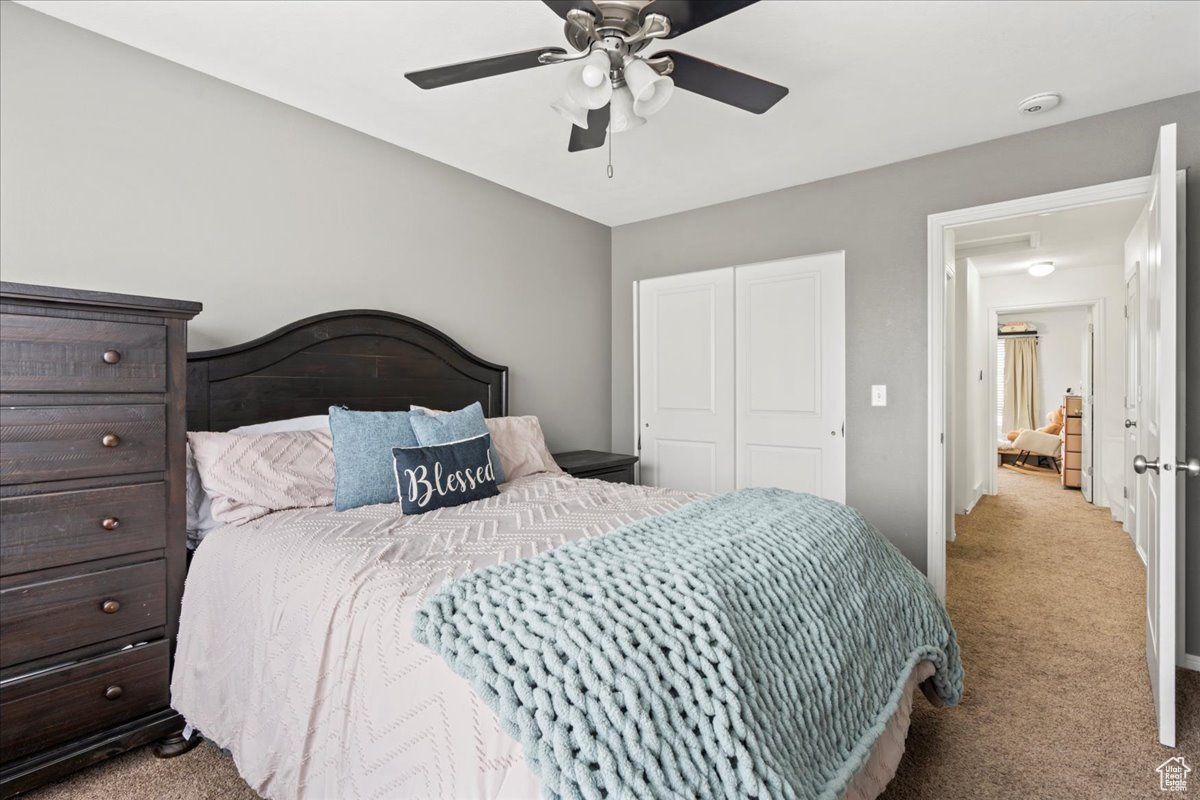 Carpeted bedroom with ceiling fan and a closet