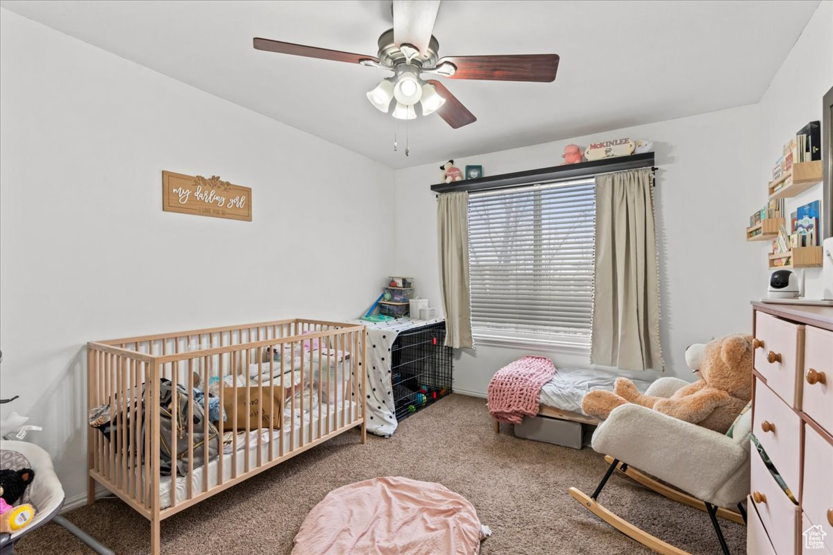 Bedroom featuring a crib, carpet floors, and ceiling fan