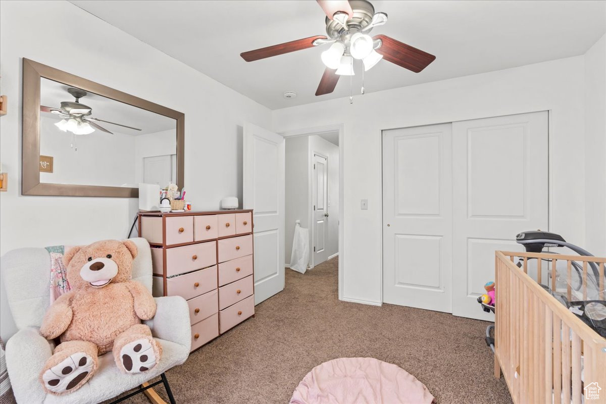 Bedroom featuring ceiling fan, a closet, light carpet, and a crib