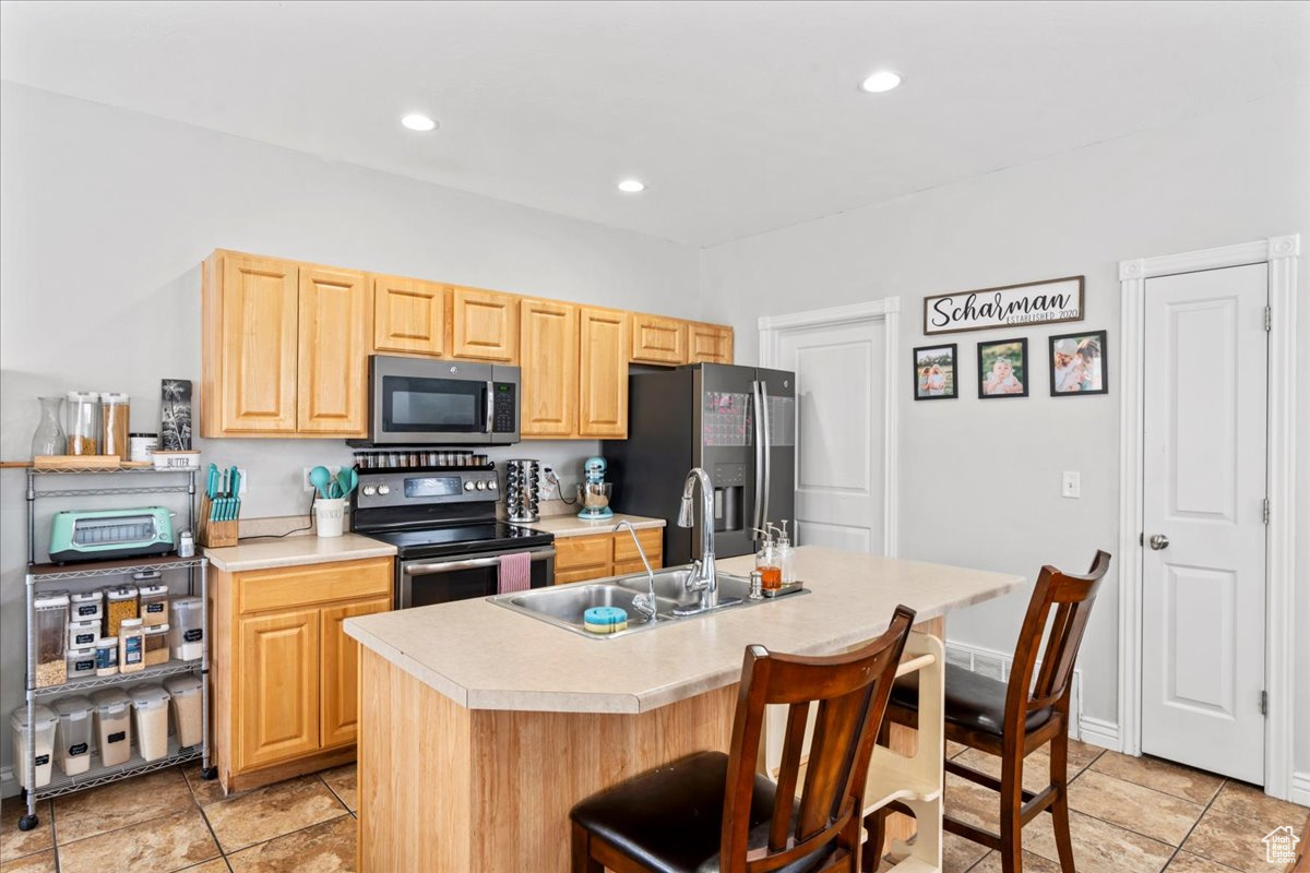 Kitchen with appliances with stainless steel finishes, light brown cabinetry, sink, a kitchen breakfast bar, and a kitchen island with sink