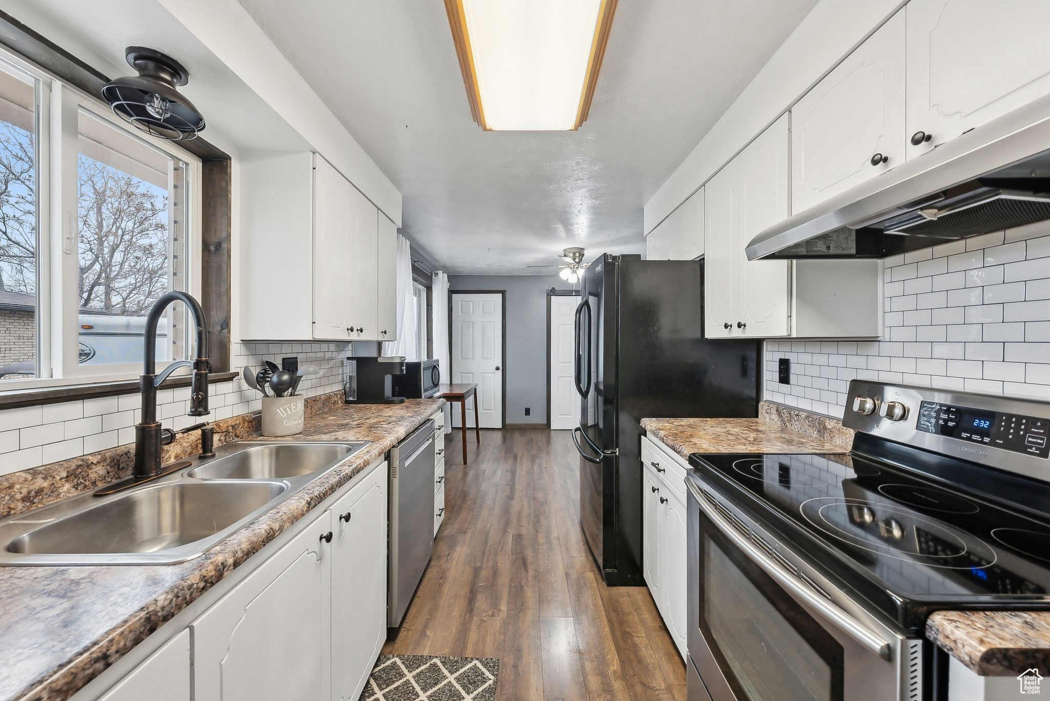 Kitchen with stainless steel appliances, sink, dark wood-type flooring, and white cabinets