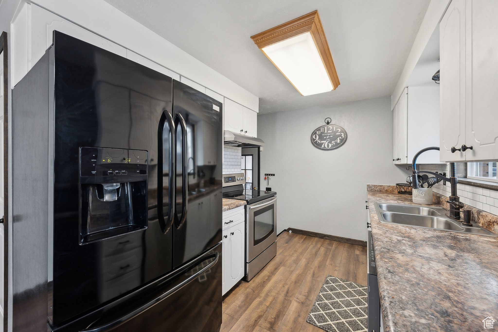 Kitchen with sink, stainless steel electric range, white cabinetry, hardwood / wood-style floors, and black fridge with ice dispenser