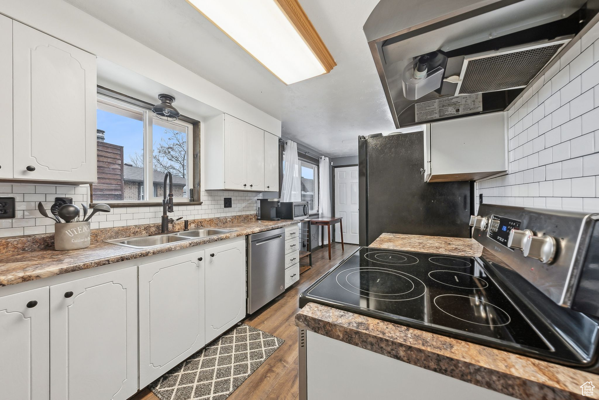 Kitchen with white cabinetry, sink, backsplash, stainless steel appliances, and dark wood-type flooring