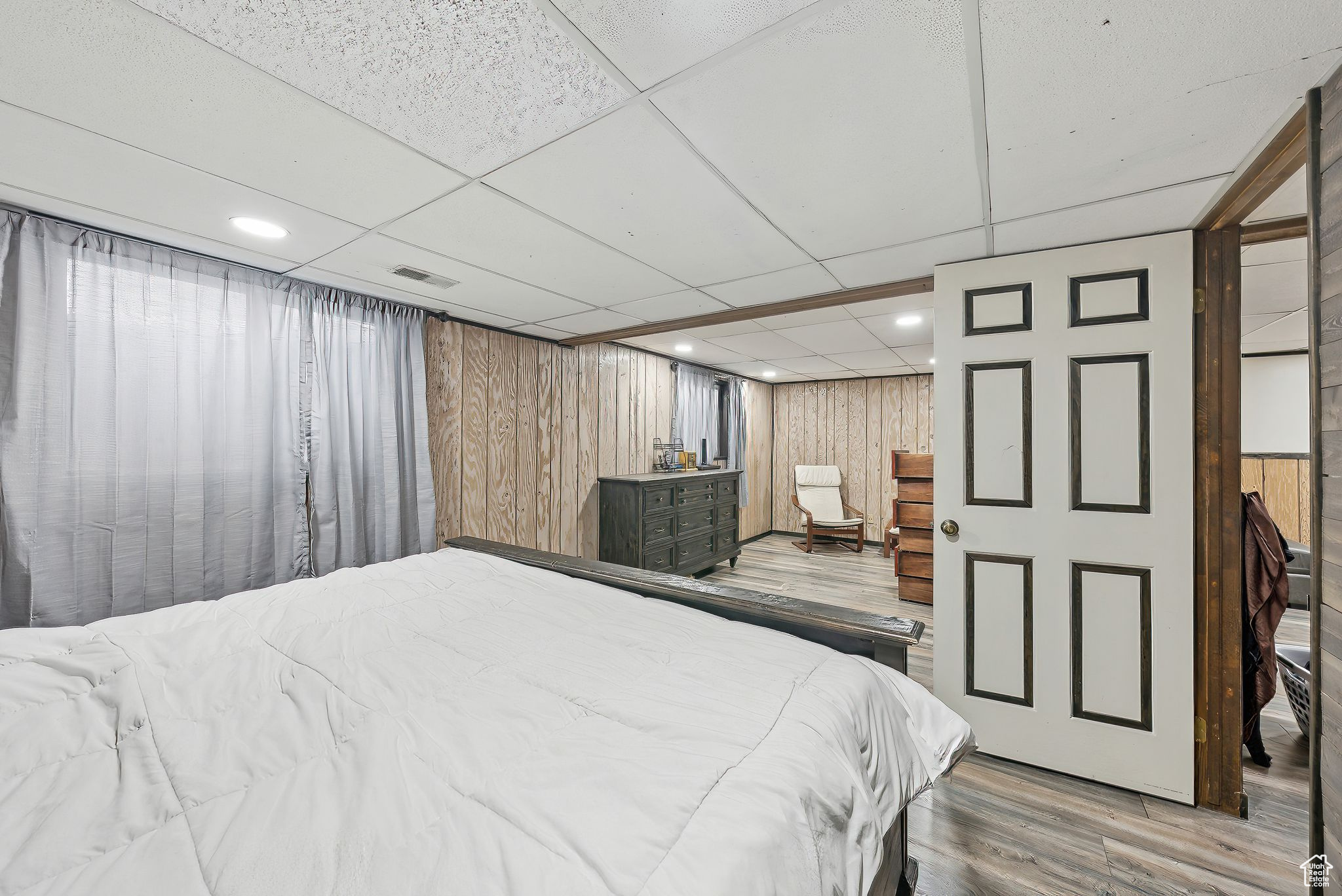 Bedroom with a drop ceiling, wooden walls, and light hardwood / wood-style flooring