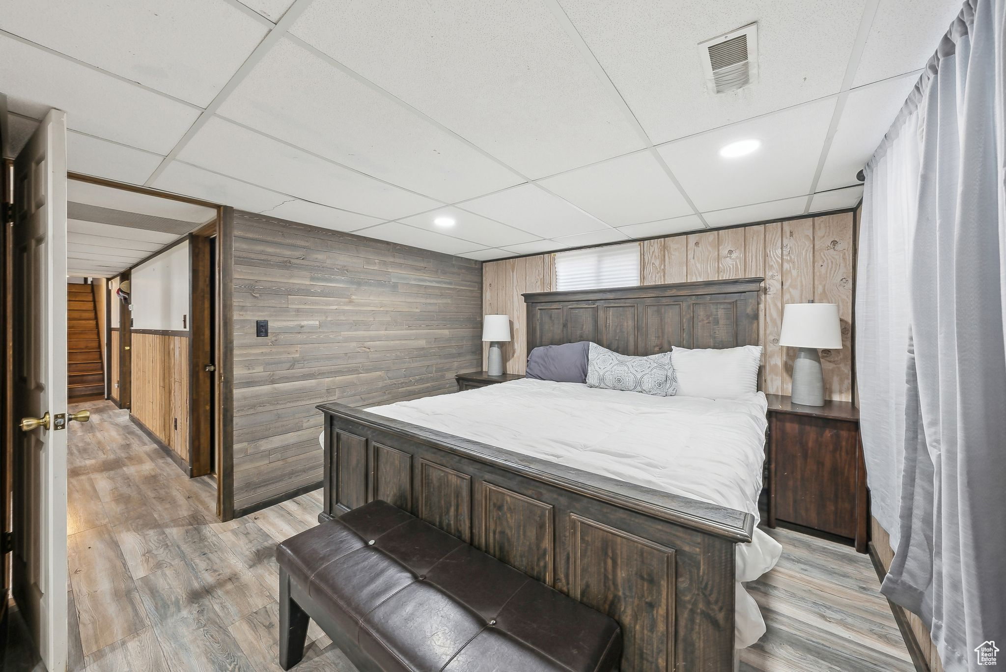 Bedroom featuring light wood-type flooring, a drop ceiling, and wooden walls