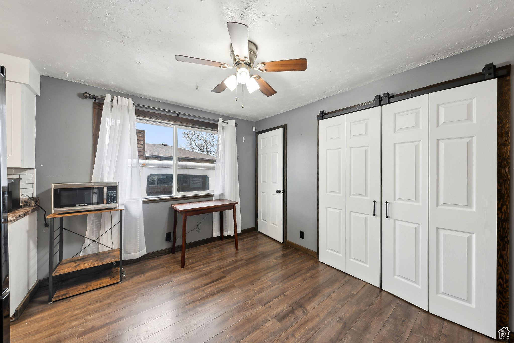 Bedroom with a barn door, dark wood-type flooring, a textured ceiling, and ceiling fan