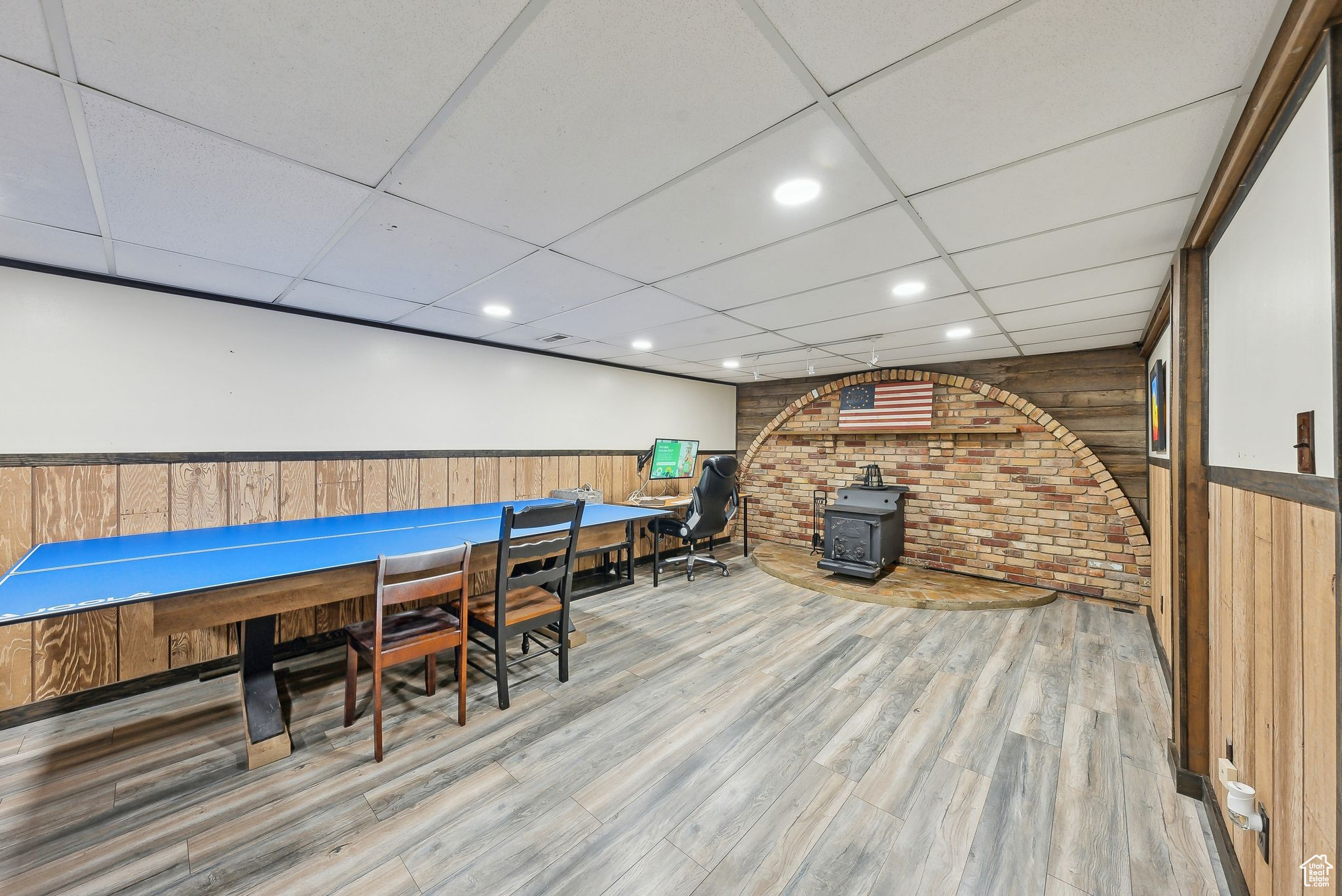 Rec room featuring a drop ceiling, hardwood / wood-style floors, brick wall, and a wood stove