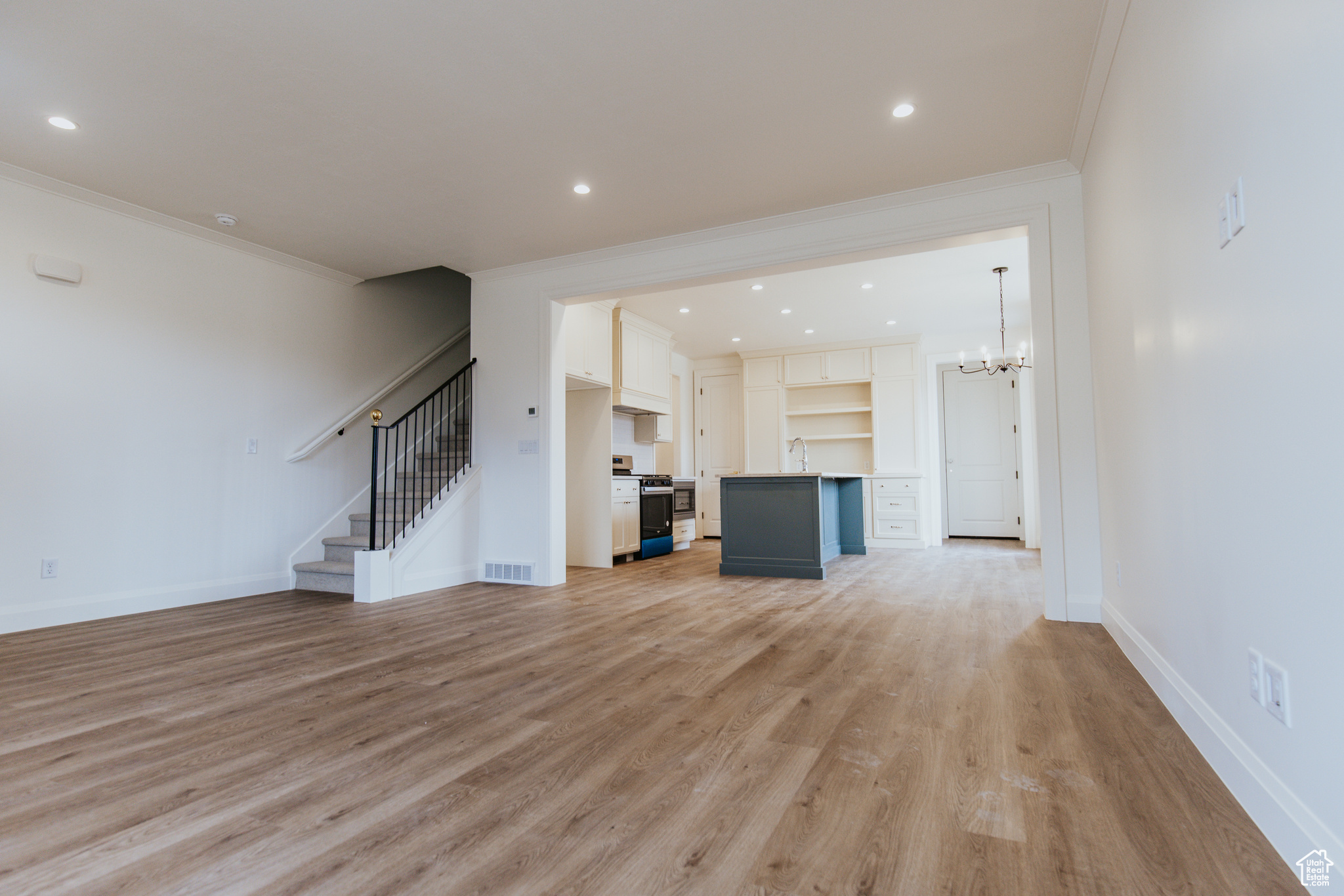 Unfurnished living room featuring sink, light hardwood / wood-style flooring, ornamental molding, and a chandelier