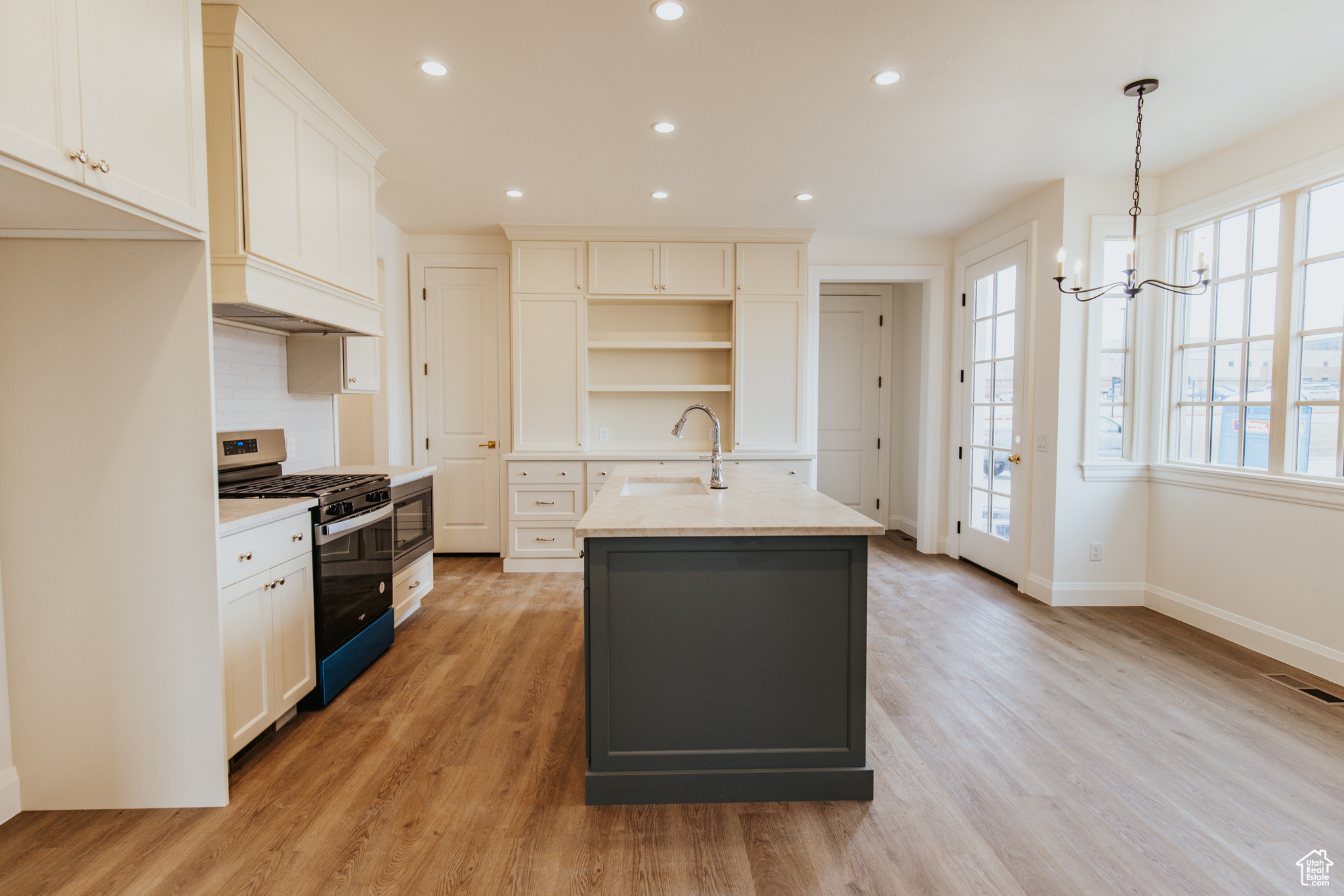 Kitchen featuring sink, stainless steel range with gas stovetop, an island with sink, white cabinets, and light wood-type flooring