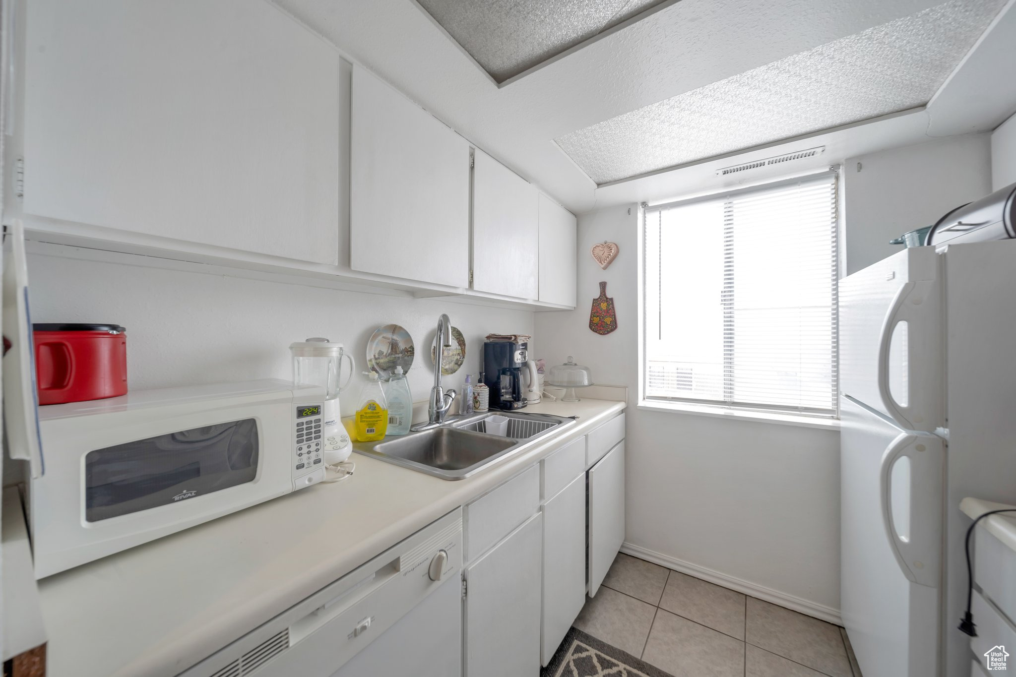 Kitchen featuring light tile patterned flooring, sink, white cabinets, and white appliances