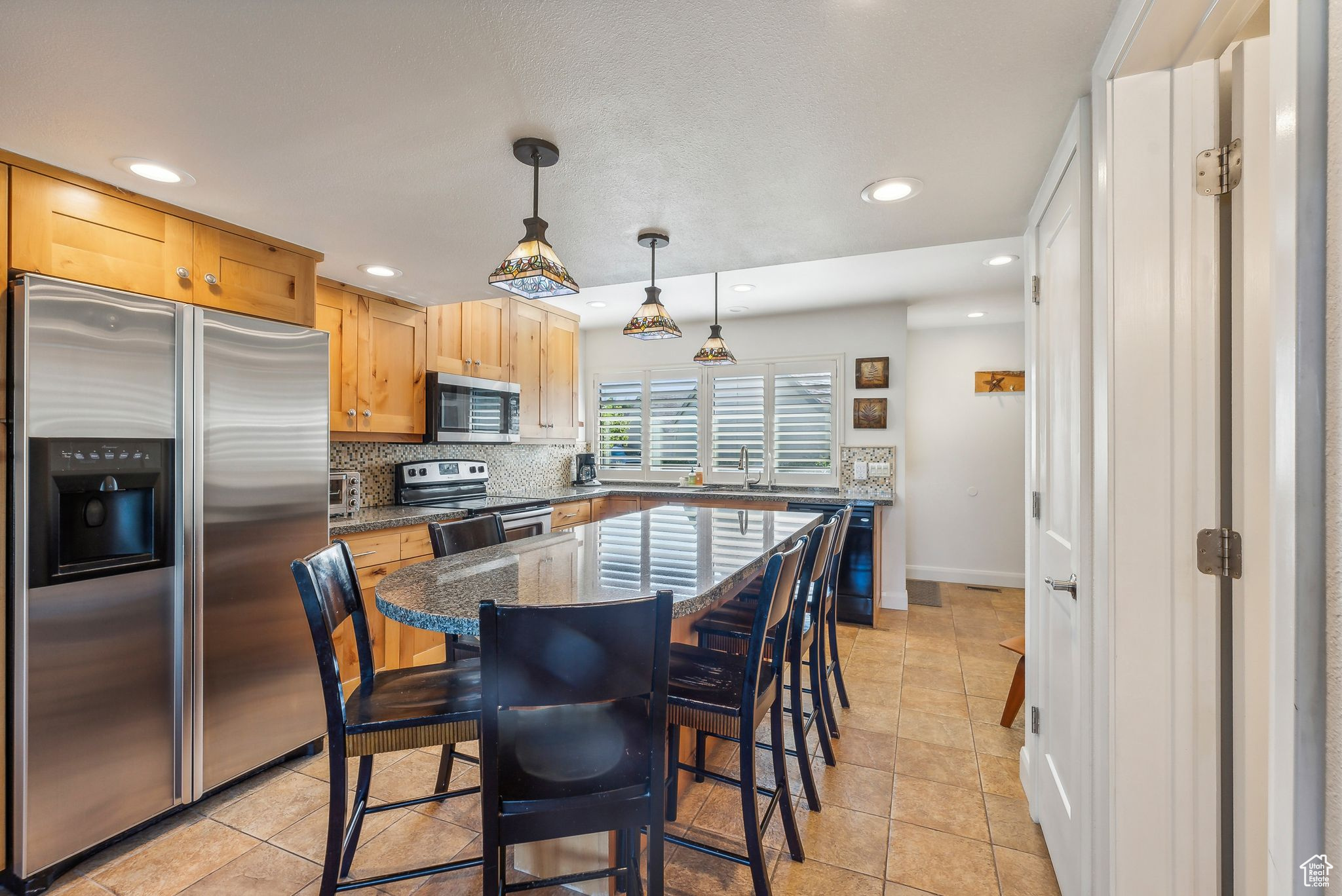 Kitchen featuring hanging light fixtures, light tile patterned floors, appliances with stainless steel finishes, a kitchen island, and dark stone counters