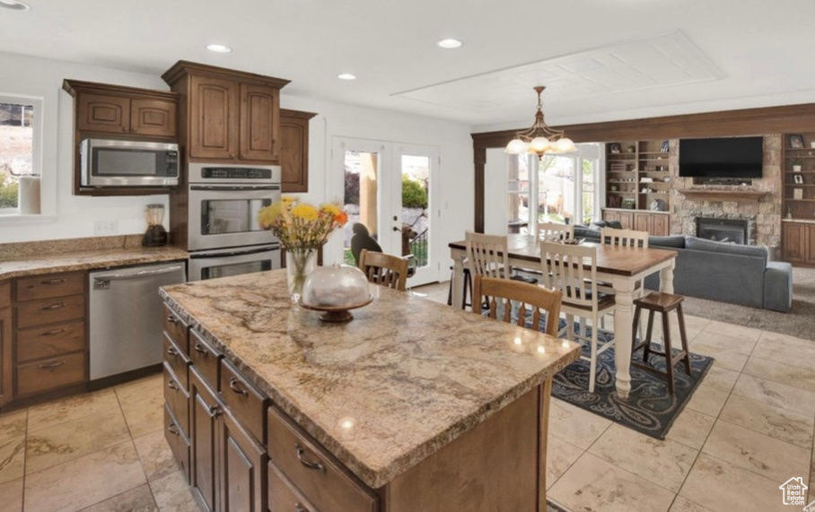 Kitchen with stainless steel appliances, a center island, a fireplace, built in shelves, and french doors