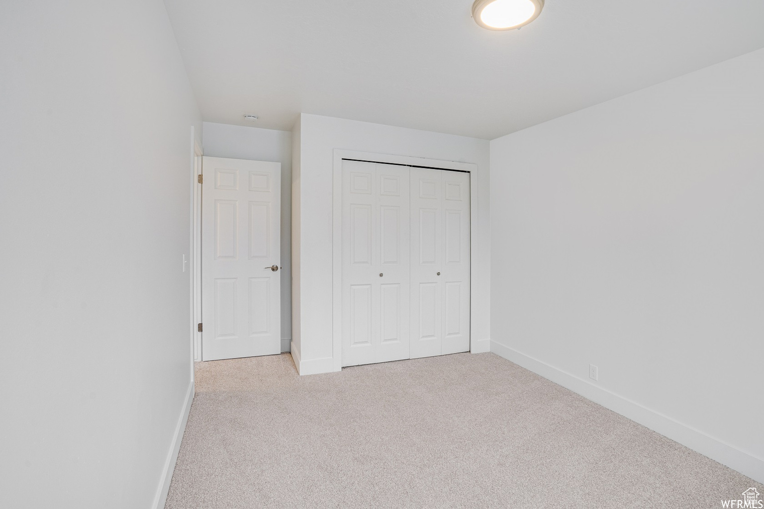 Unfurnished bedroom with light colored carpet and a closet