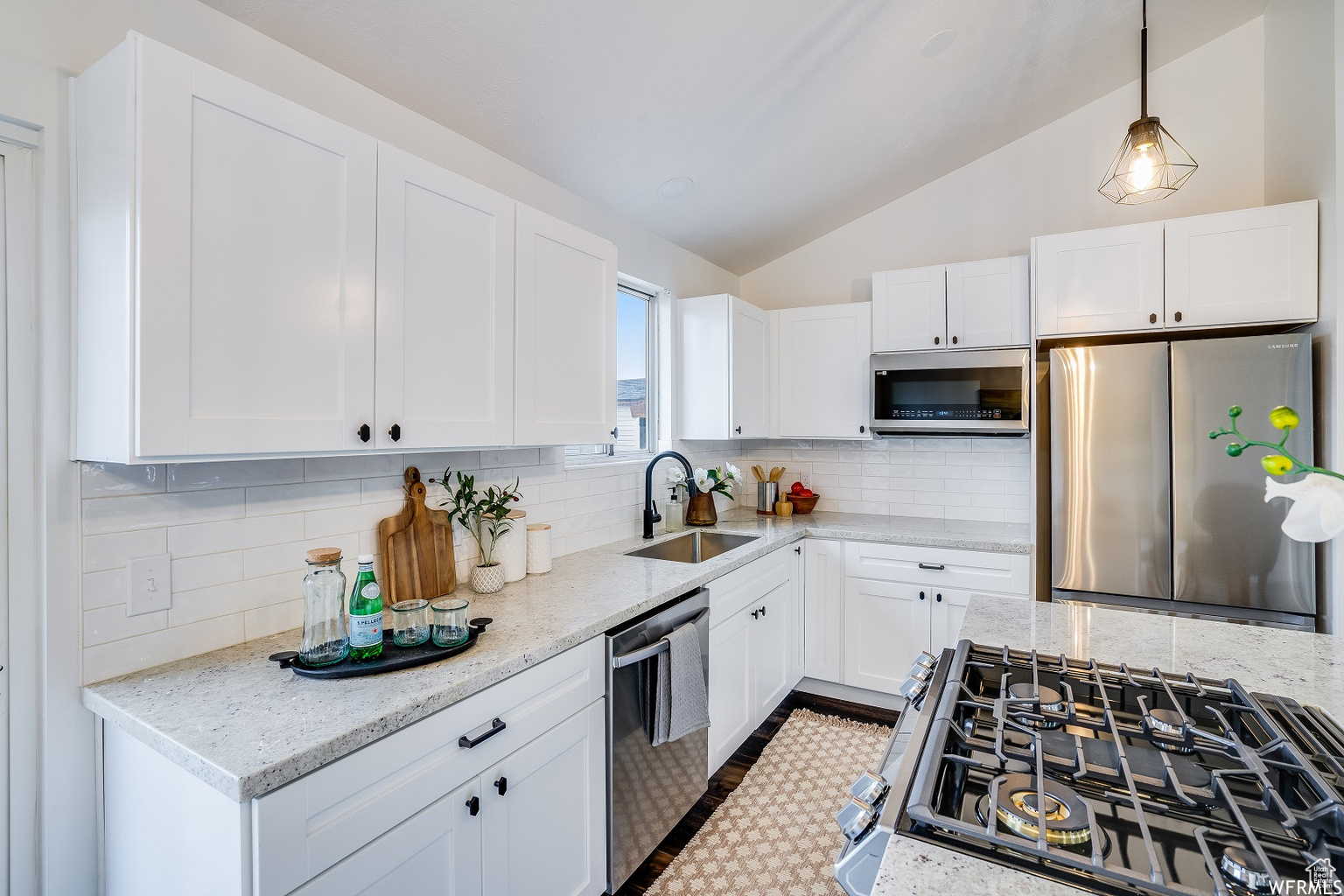 Kitchen with sink, stainless steel appliances, light stone counters, tasteful backsplash, and vaulted ceiling