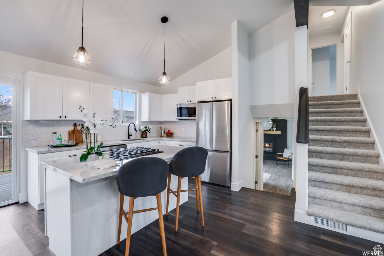 Kitchen featuring sink, white cabinetry, tasteful backsplash, decorative light fixtures, and stainless steel appliances