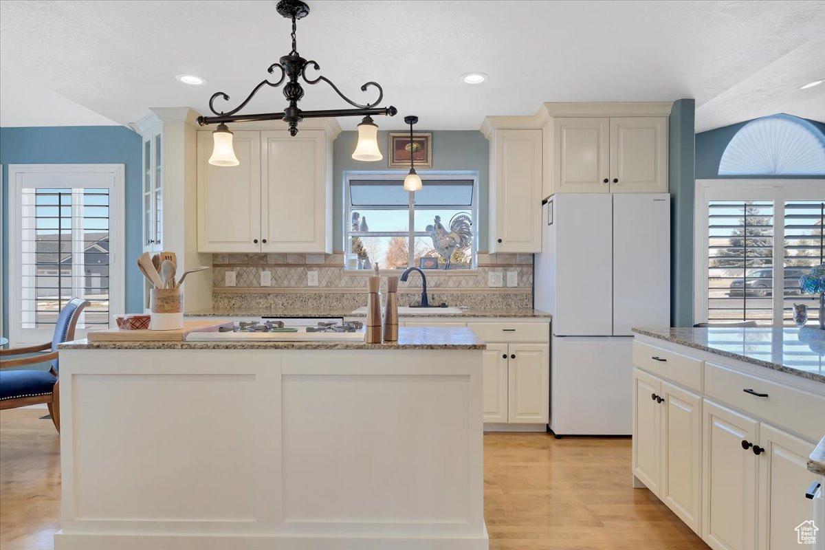 Kitchen featuring white refrigerator, tasteful backsplash, a wealth of natural light, and decorative light fixtures