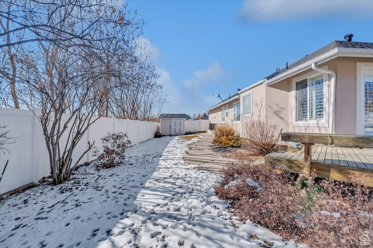 Yard layered in snow with a storage shed and a deck