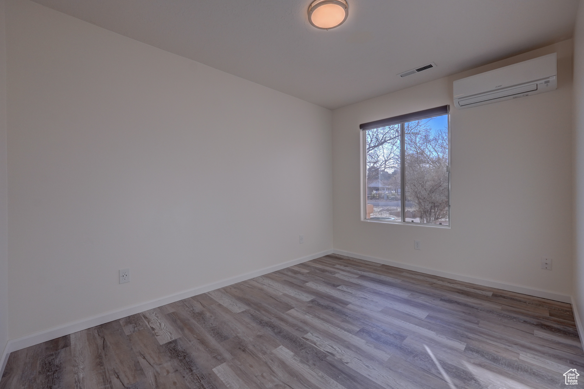 Empty room featuring light wood-type flooring and an AC wall unit