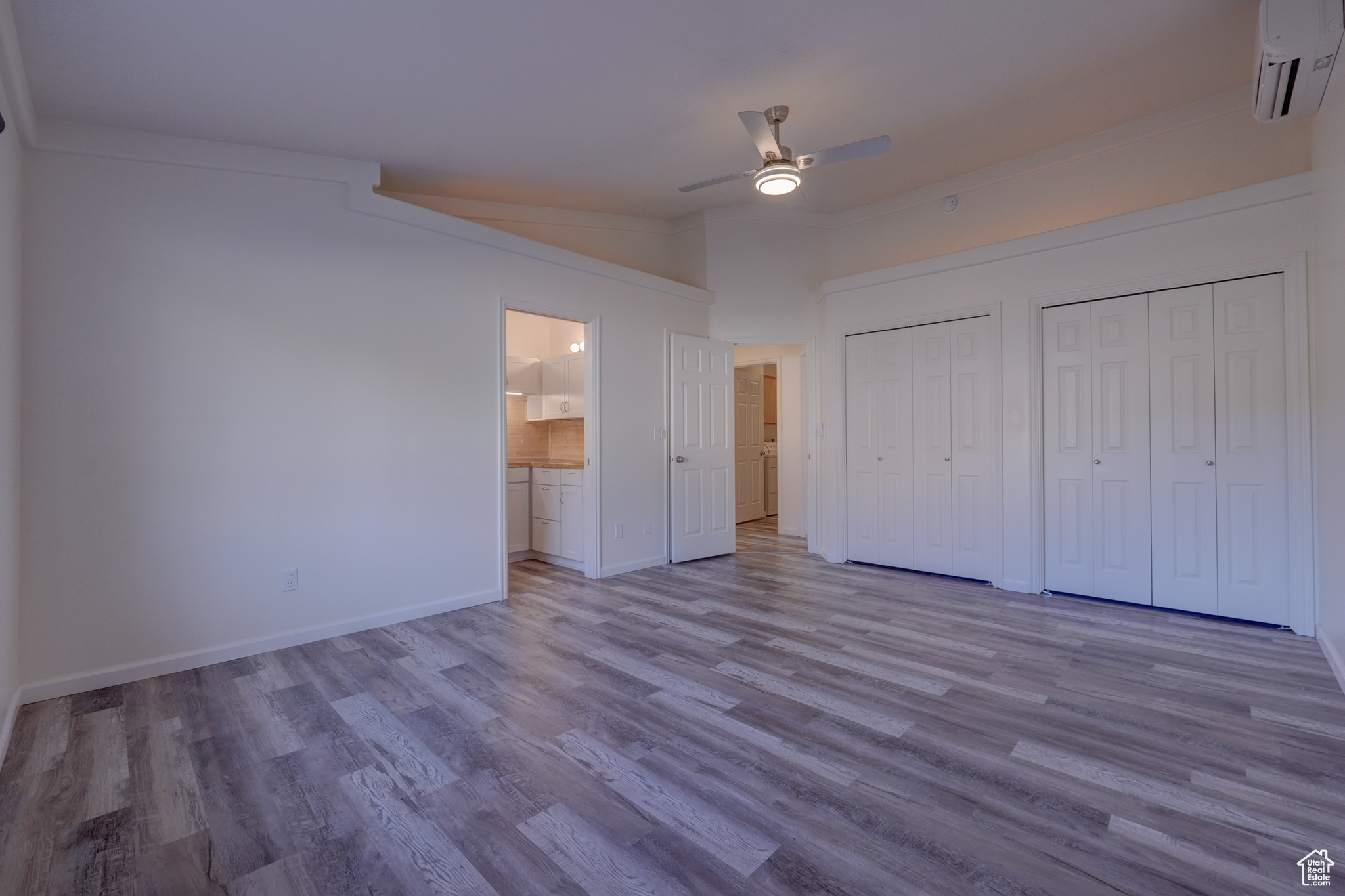 Unfurnished bedroom with connected bathroom, a wall mounted air conditioner, ceiling fan, multiple closets, and light wood-type flooring