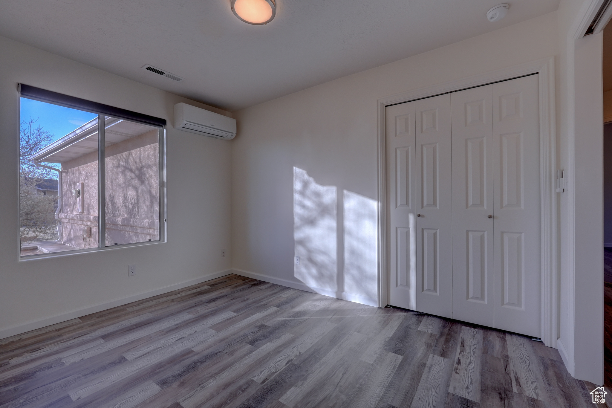 Unfurnished bedroom with light wood-type flooring, a wall unit AC, and a closet