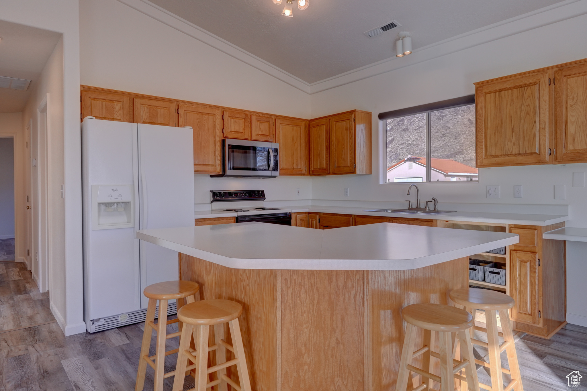 Kitchen featuring range with electric cooktop, white refrigerator with ice dispenser, sink, and a breakfast bar area