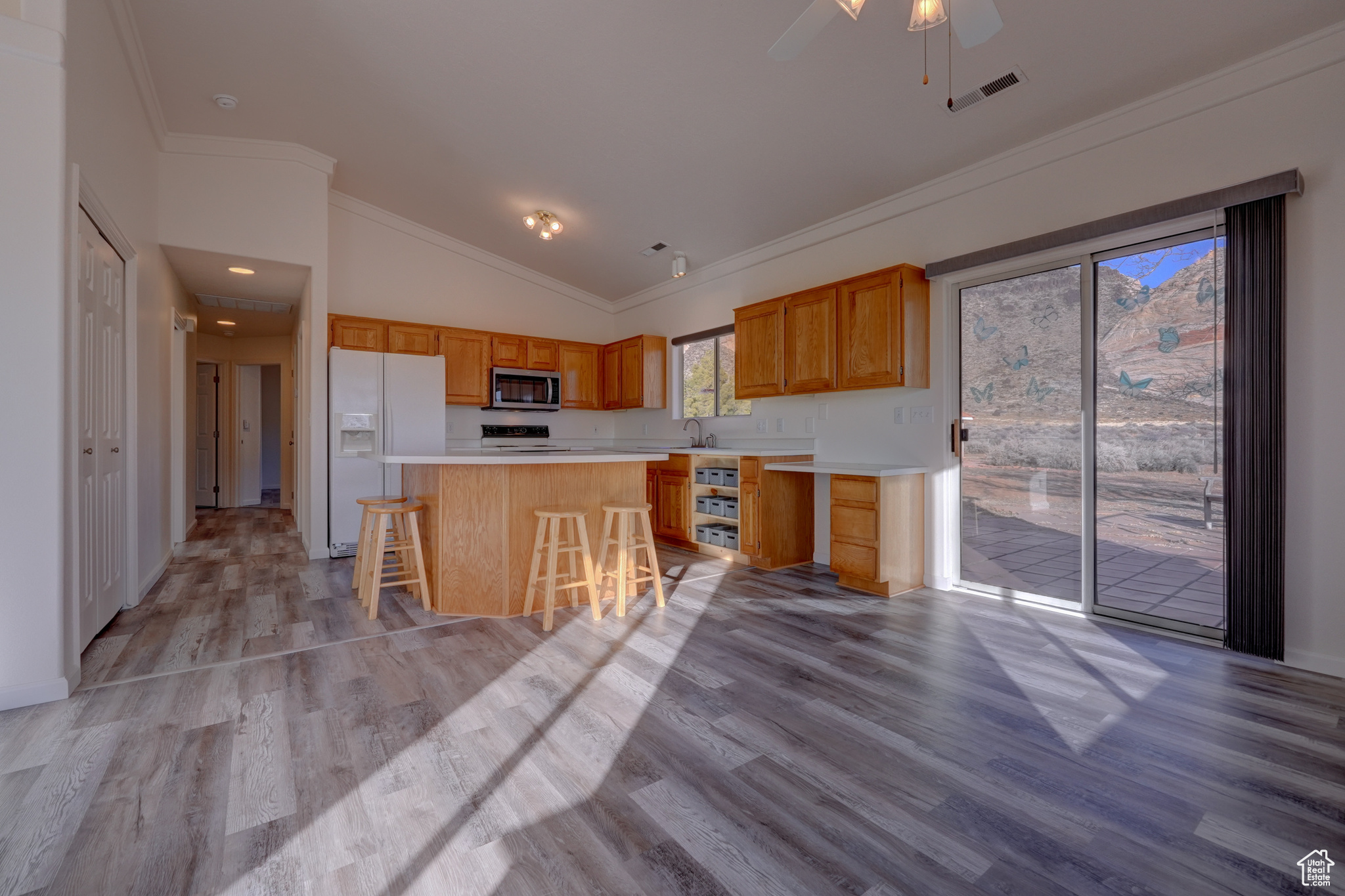 Kitchen with a breakfast bar, white refrigerator with ice dispenser, light hardwood / wood-style floors, a kitchen island, and vaulted ceiling