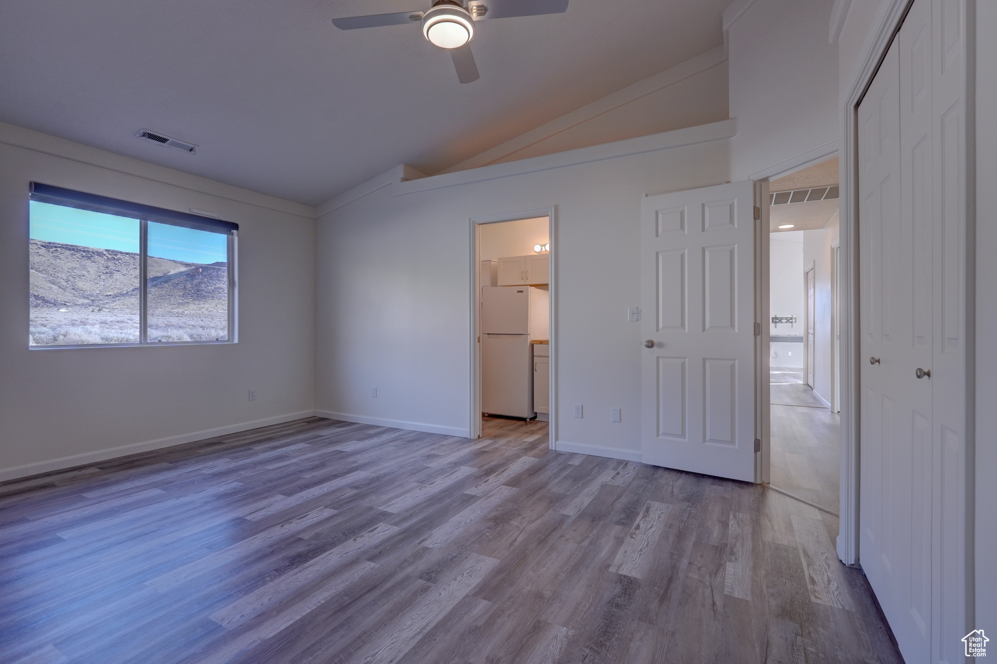 Unfurnished bedroom featuring vaulted ceiling, a closet, white refrigerator, ceiling fan, and light hardwood / wood-style flooring