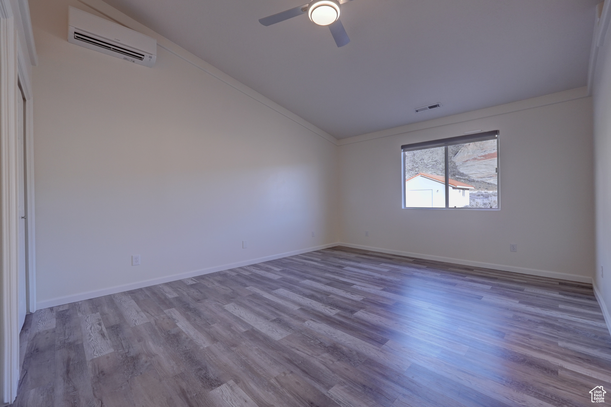 Empty room with vaulted ceiling, a wall mounted AC, ceiling fan, light hardwood / wood-style floors, and crown molding