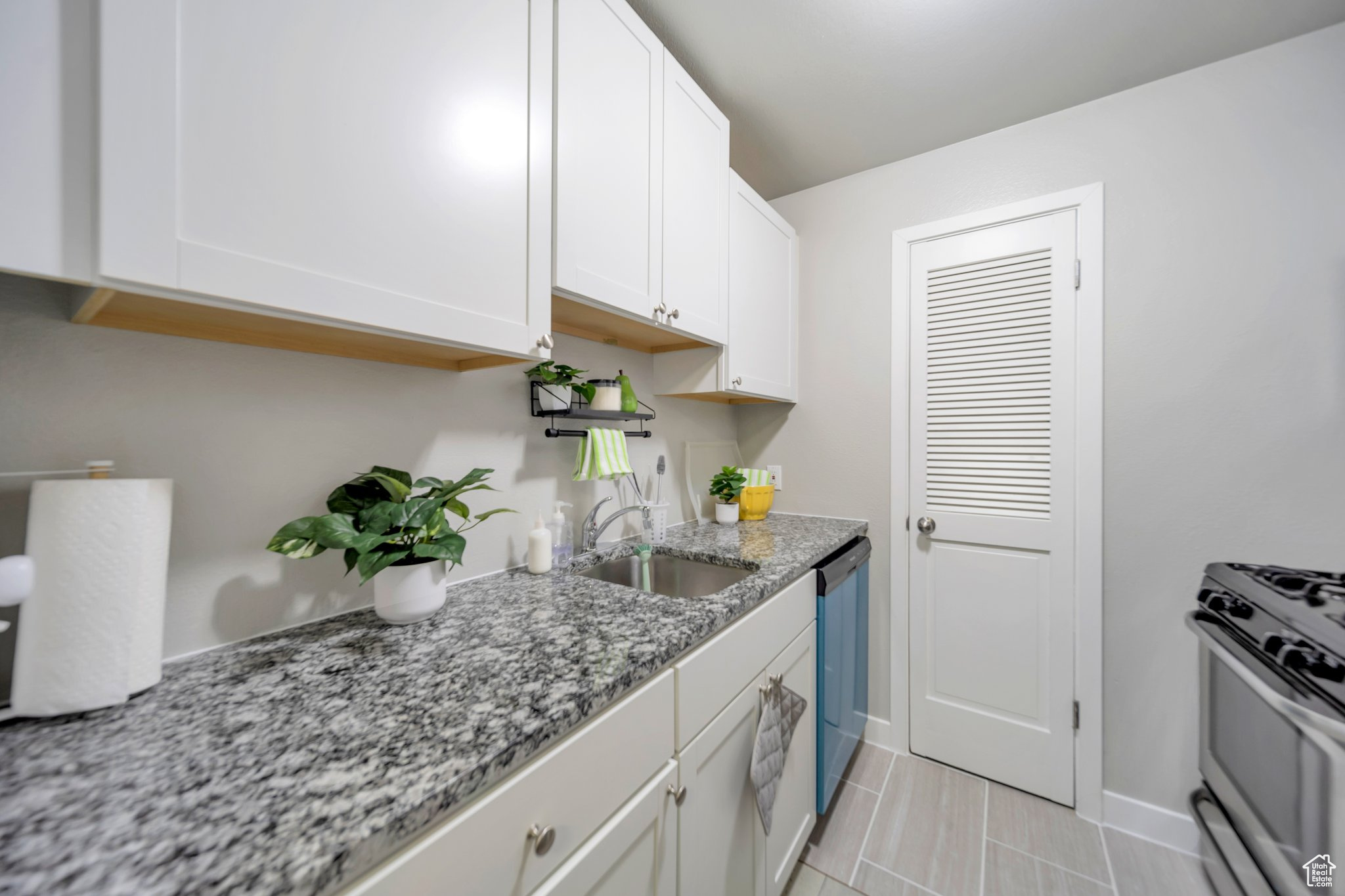 Kitchen with white cabinetry, sink, light tile patterned floors, light stone counters, and stainless steel appliances