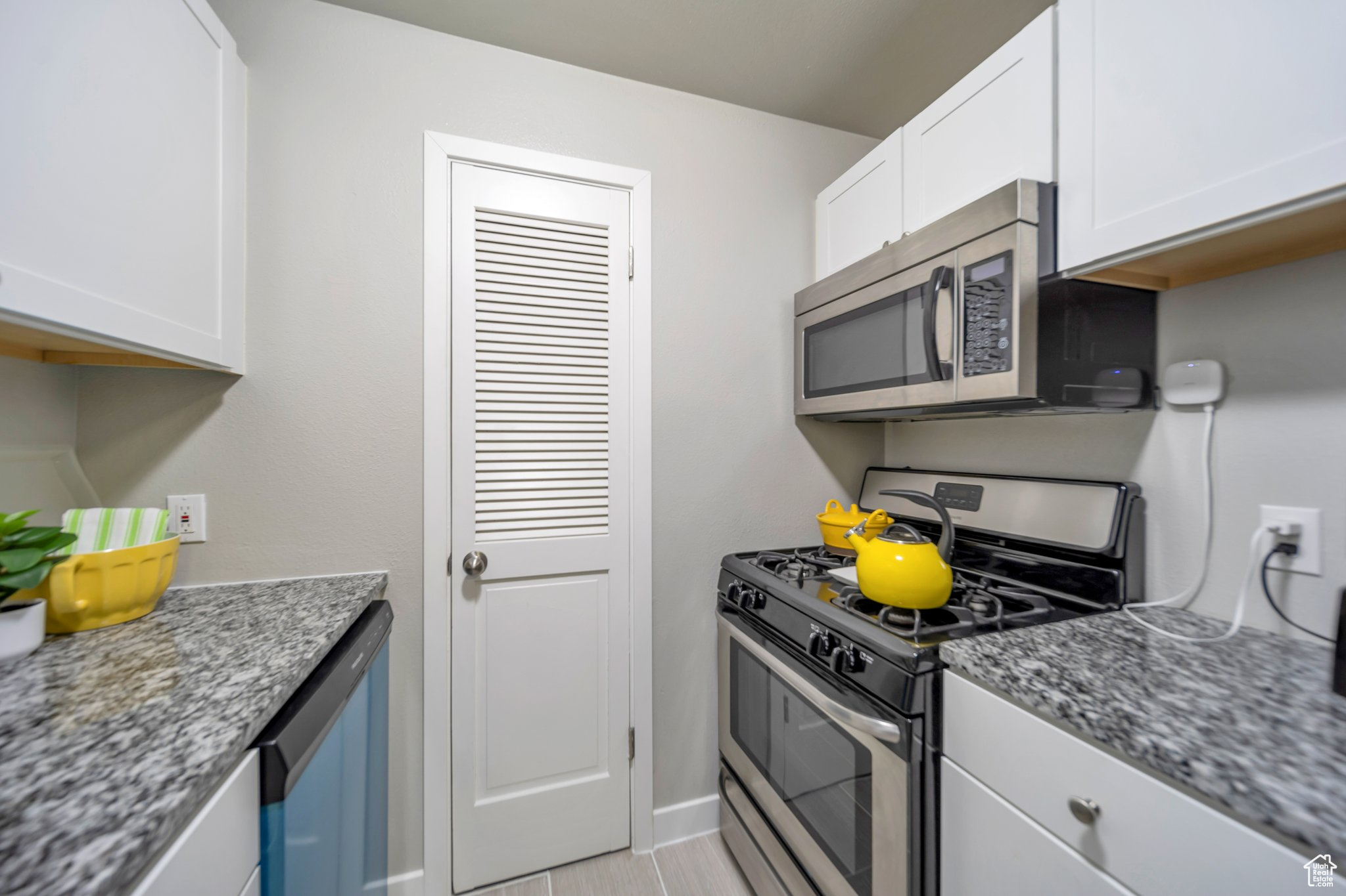 Kitchen with light tile patterned flooring, stainless steel appliances, white cabinets, and stone counters