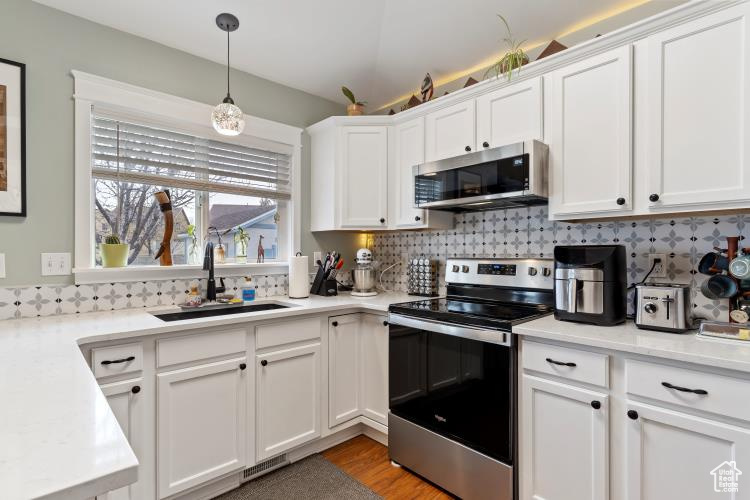 Kitchen with decorative light fixtures, white cabinets, decorative backsplash, and stainless steel appliances