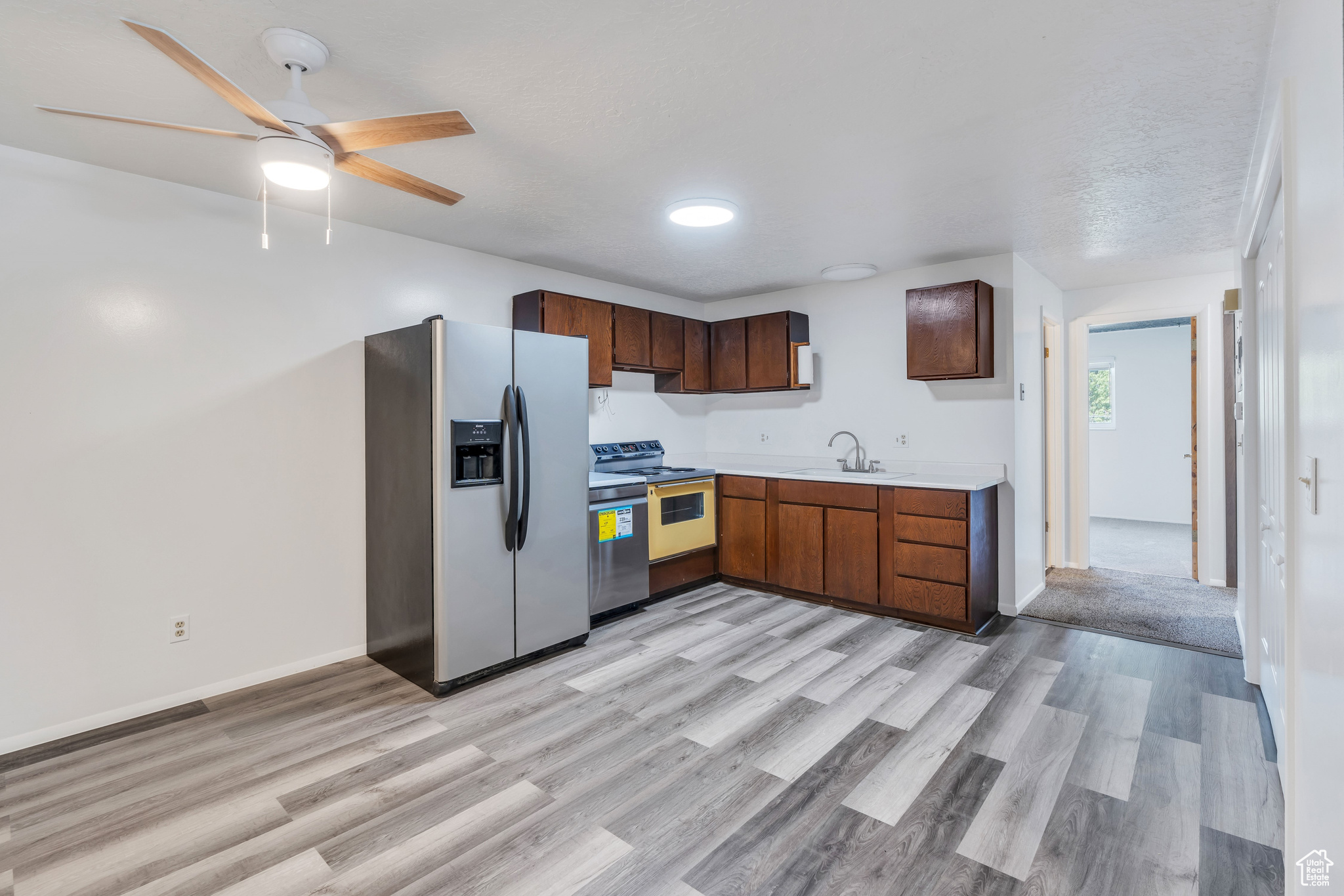 Kitchen featuring sink, ceiling fan, light hardwood / wood-style floors, stainless steel appliances, and a textured ceiling