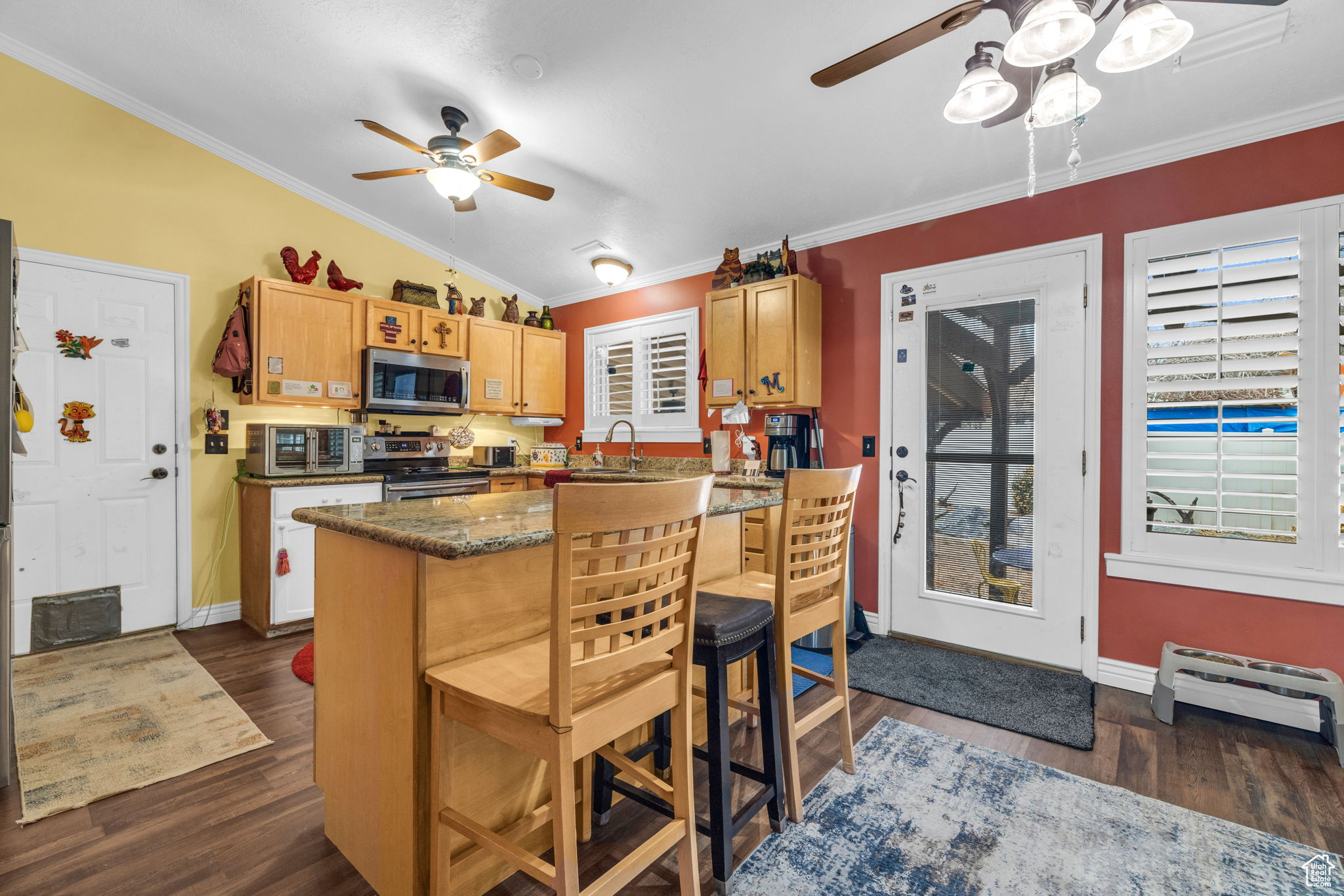 Kitchen featuring a breakfast bar, dark hardwood / wood-style floors, dark stone counters, stainless steel appliances, and crown molding