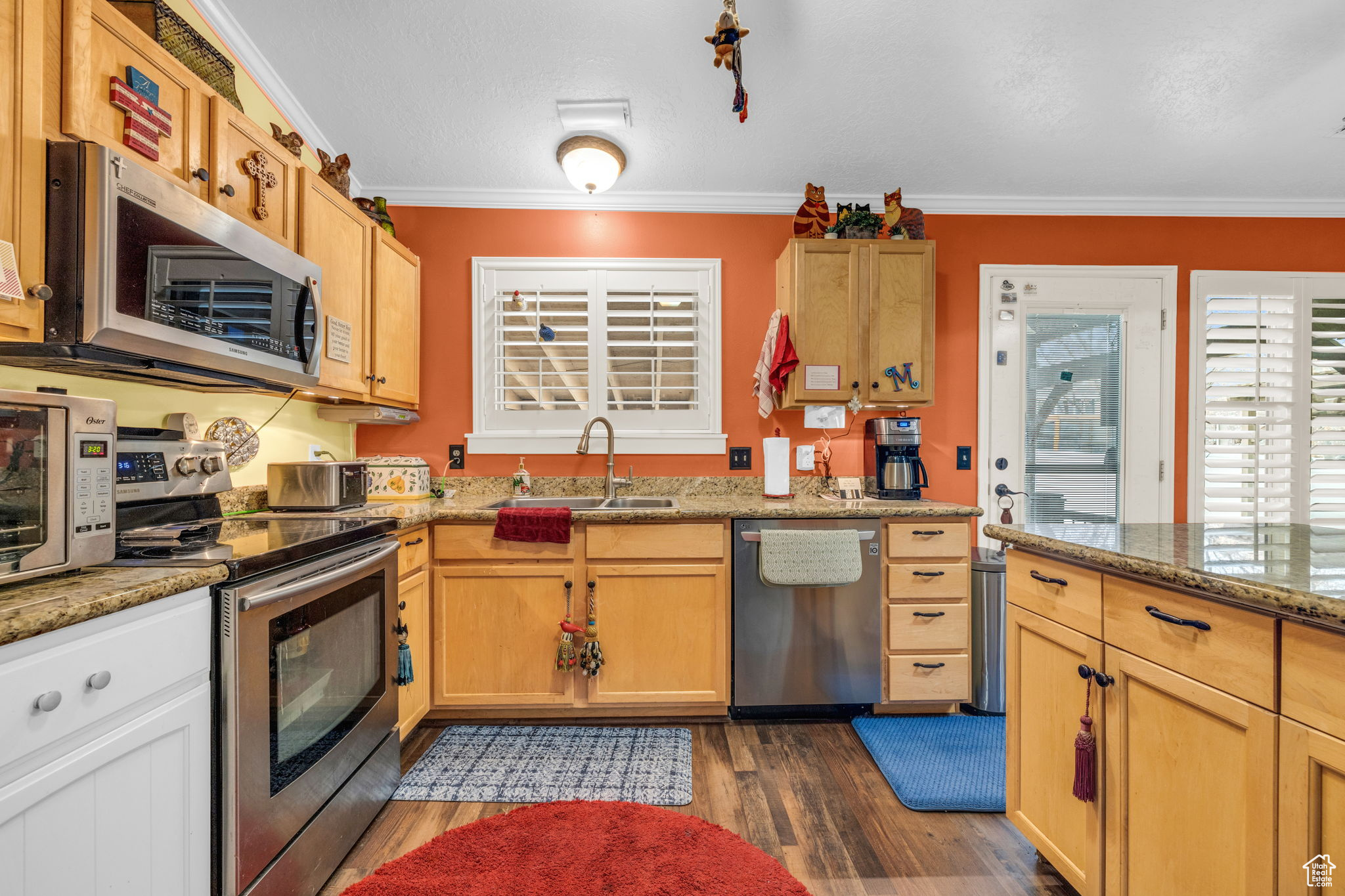 Kitchen with stainless steel appliances, crown molding, light stone countertops, and sink