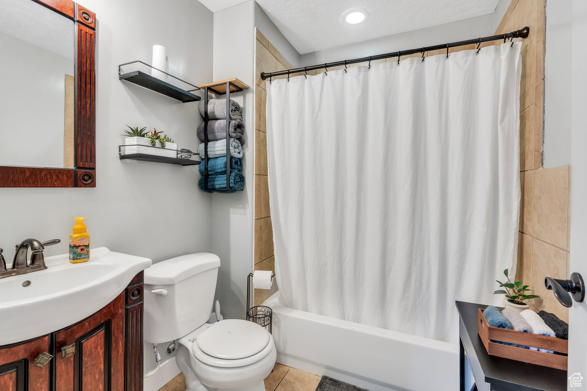 Full bathroom with tile patterned flooring, vanity, toilet, shower / bathtub combination with curtain, and a textured ceiling