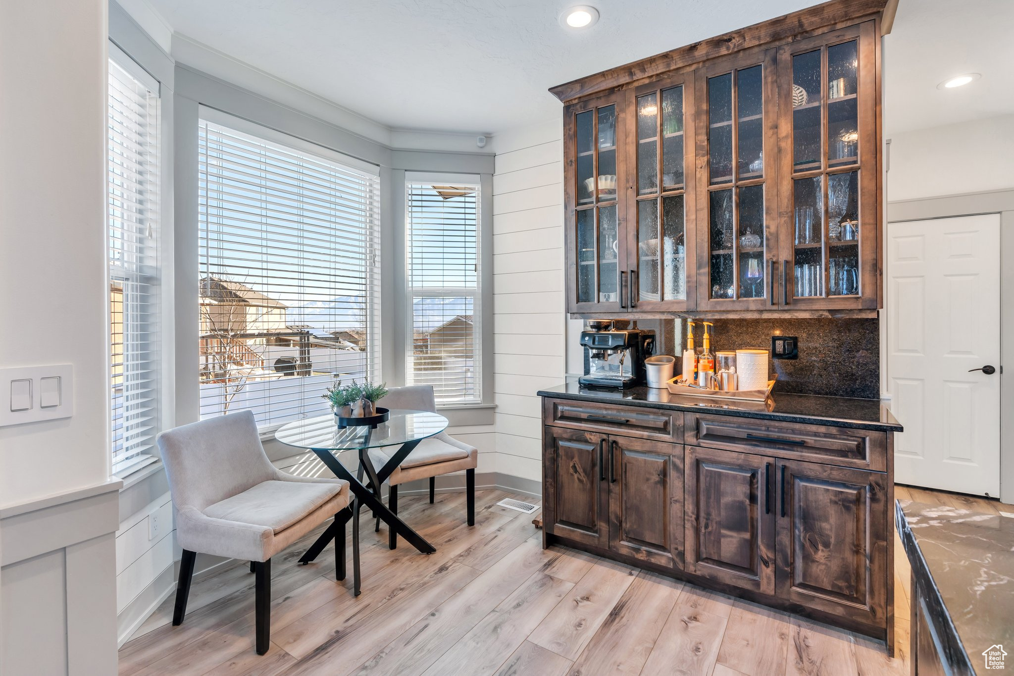 Bar with dark stone countertops, ornamental molding, dark brown cabinets, and light hardwood / wood-style floors