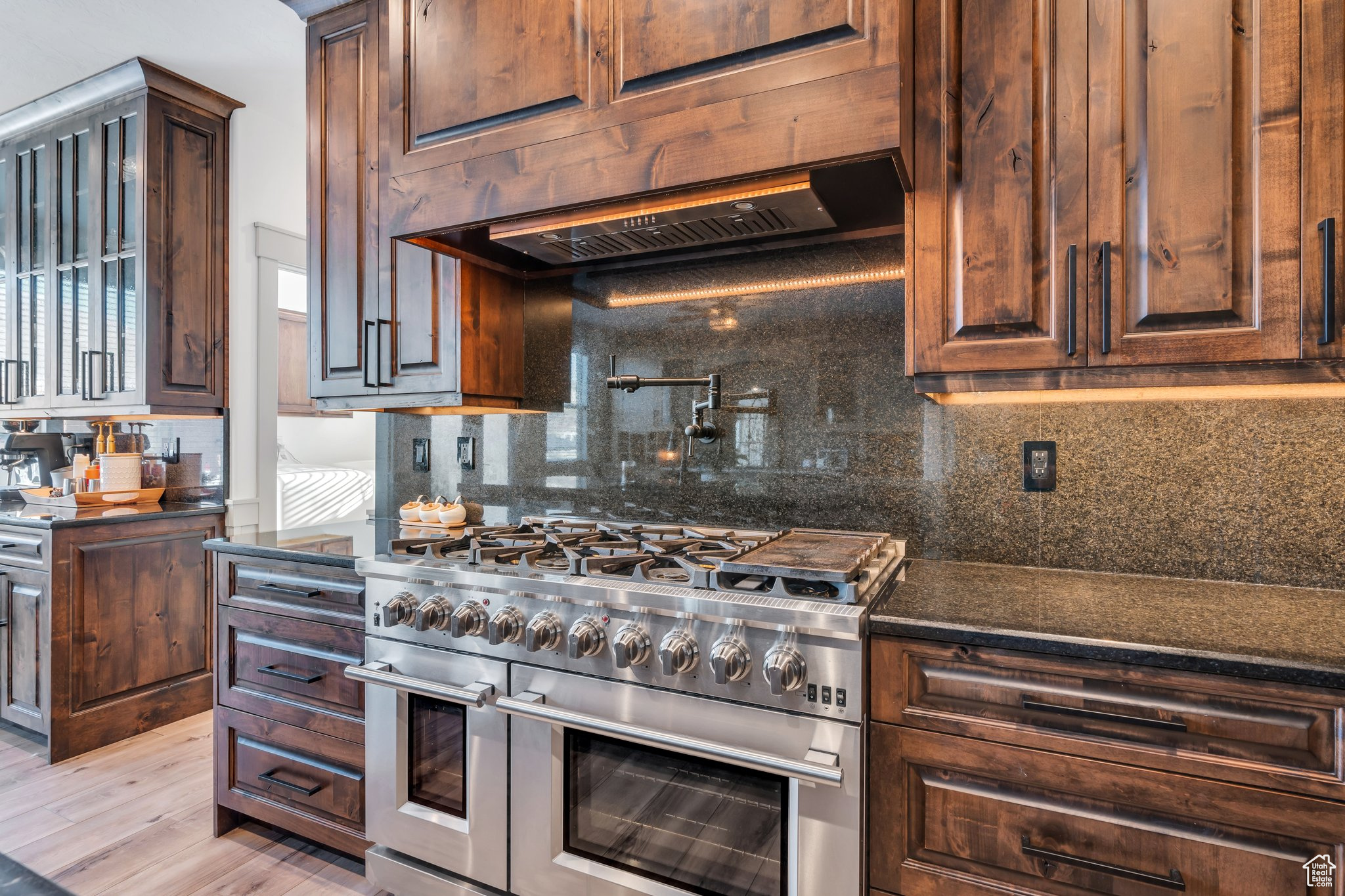 Kitchen featuring premium range hood, double oven range, light hardwood / wood-style floors, and backsplash