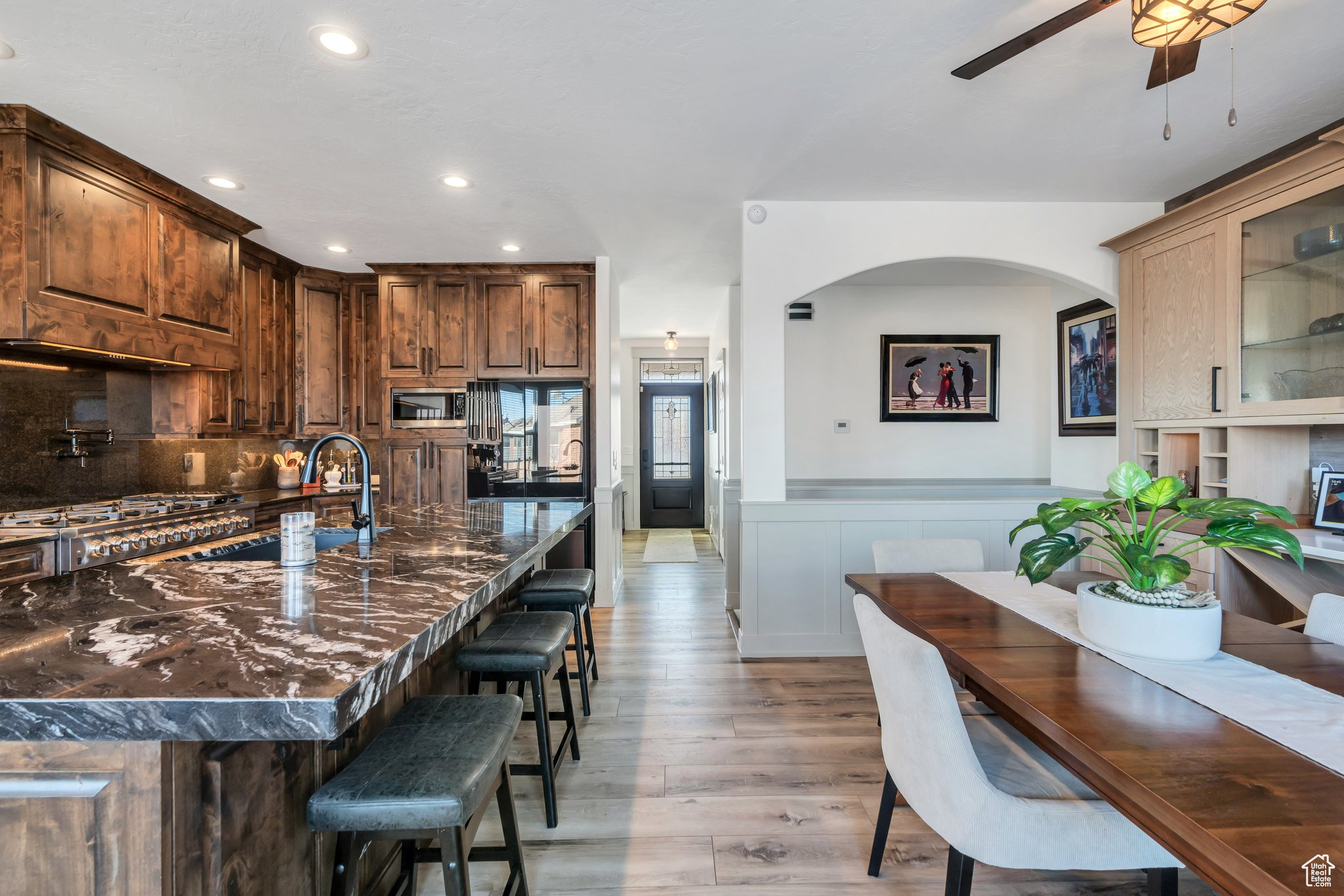 Kitchen featuring appliances with stainless steel finishes, a kitchen breakfast bar, light hardwood / wood-style floors, decorative backsplash, and dark stone counters