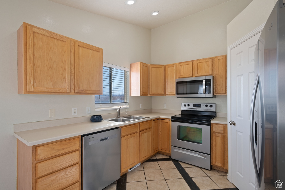 Kitchen with light tile patterned flooring, appliances with stainless steel finishes, sink, and light brown cabinets